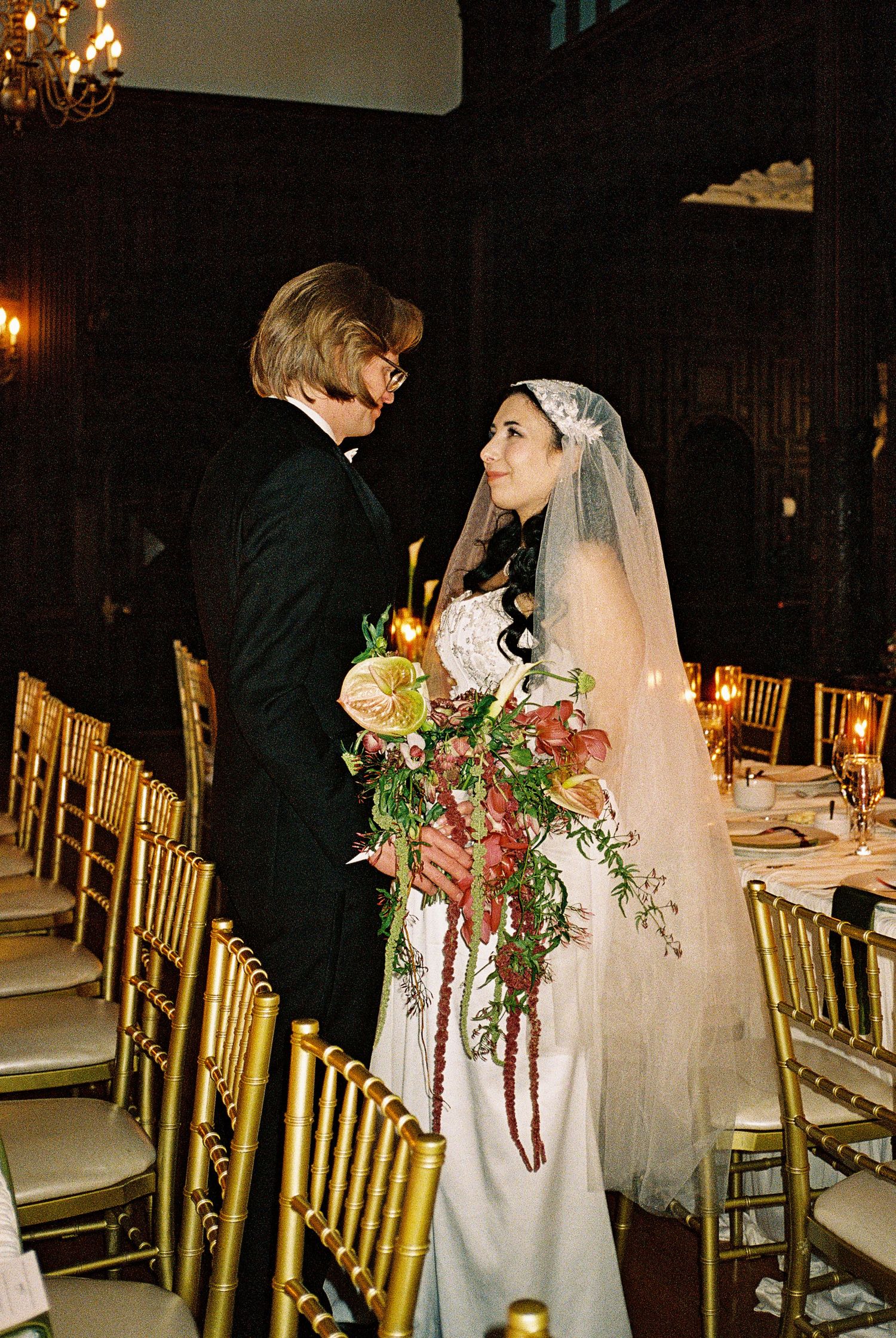 Elegant wedding reception scene with gold chairs and romantic candlelight in a grand ballroom setting.