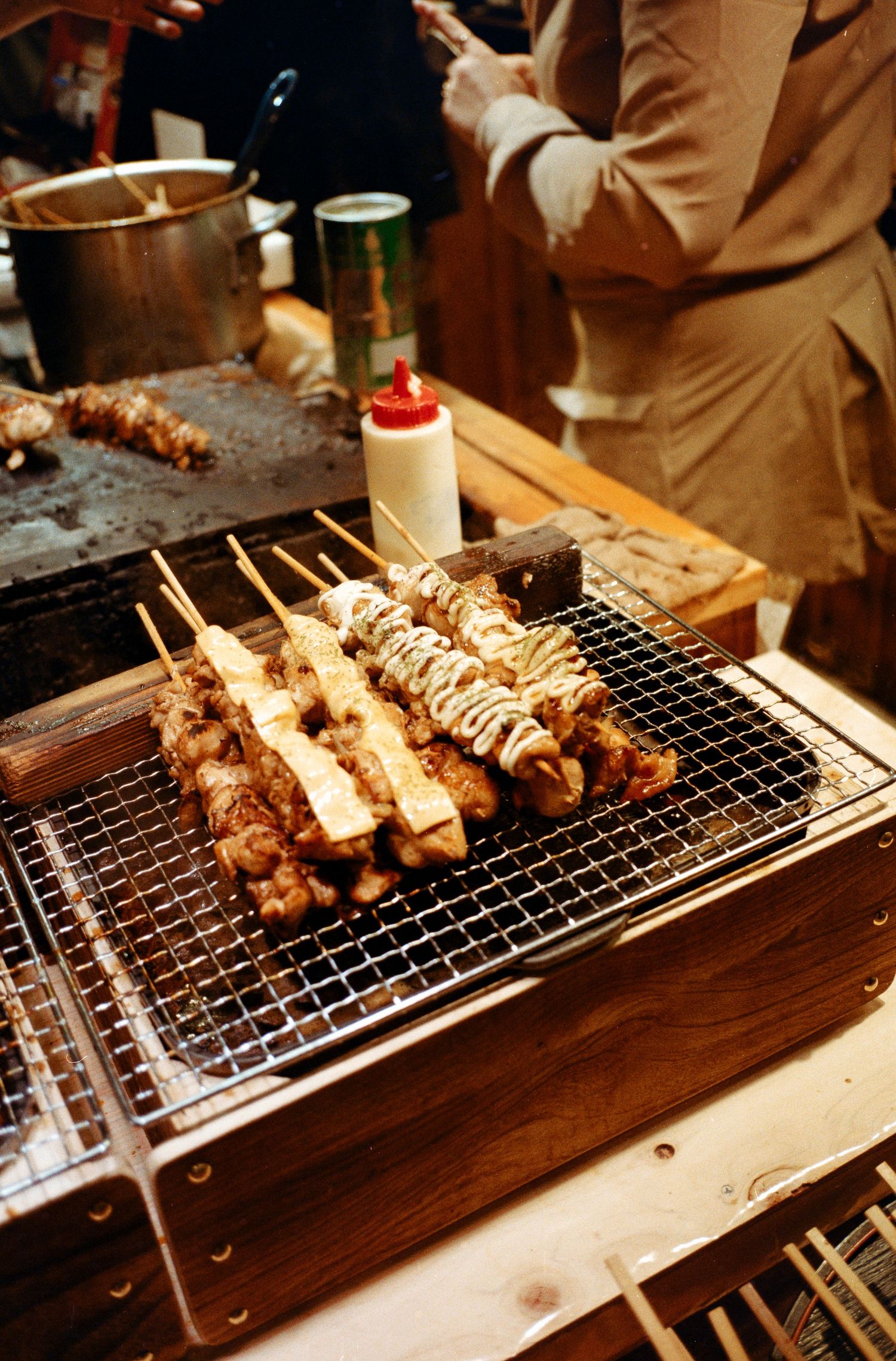 Yakitori skewers grilling over charcoal at a Japanese food stall.