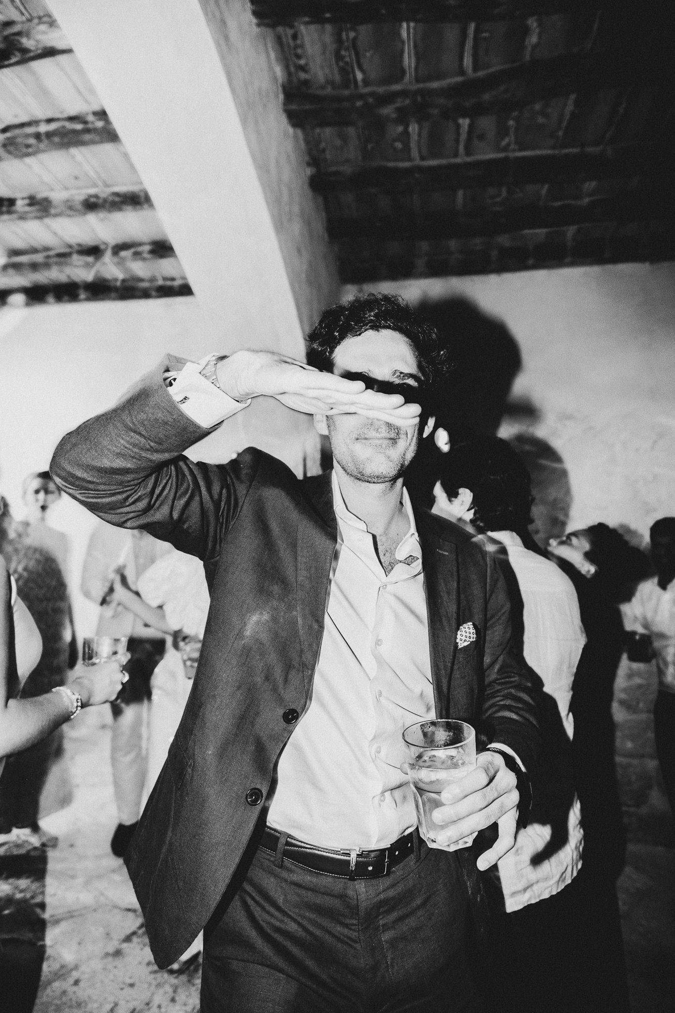 Party guest in dark blazer dancing with drink in hand at reception celebration.