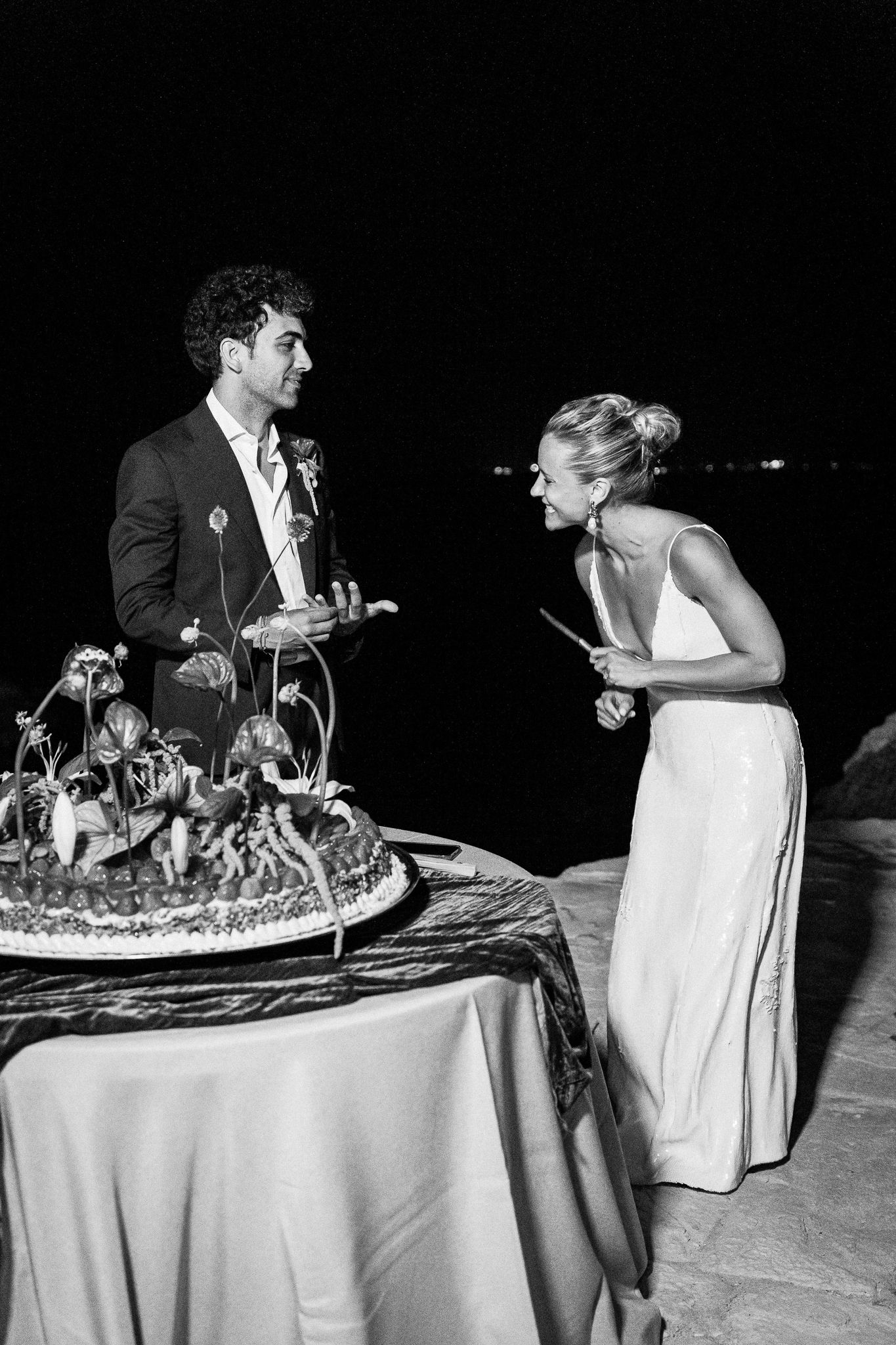 Couple cutting their ornate wedding cake together in elegant black and white photography.