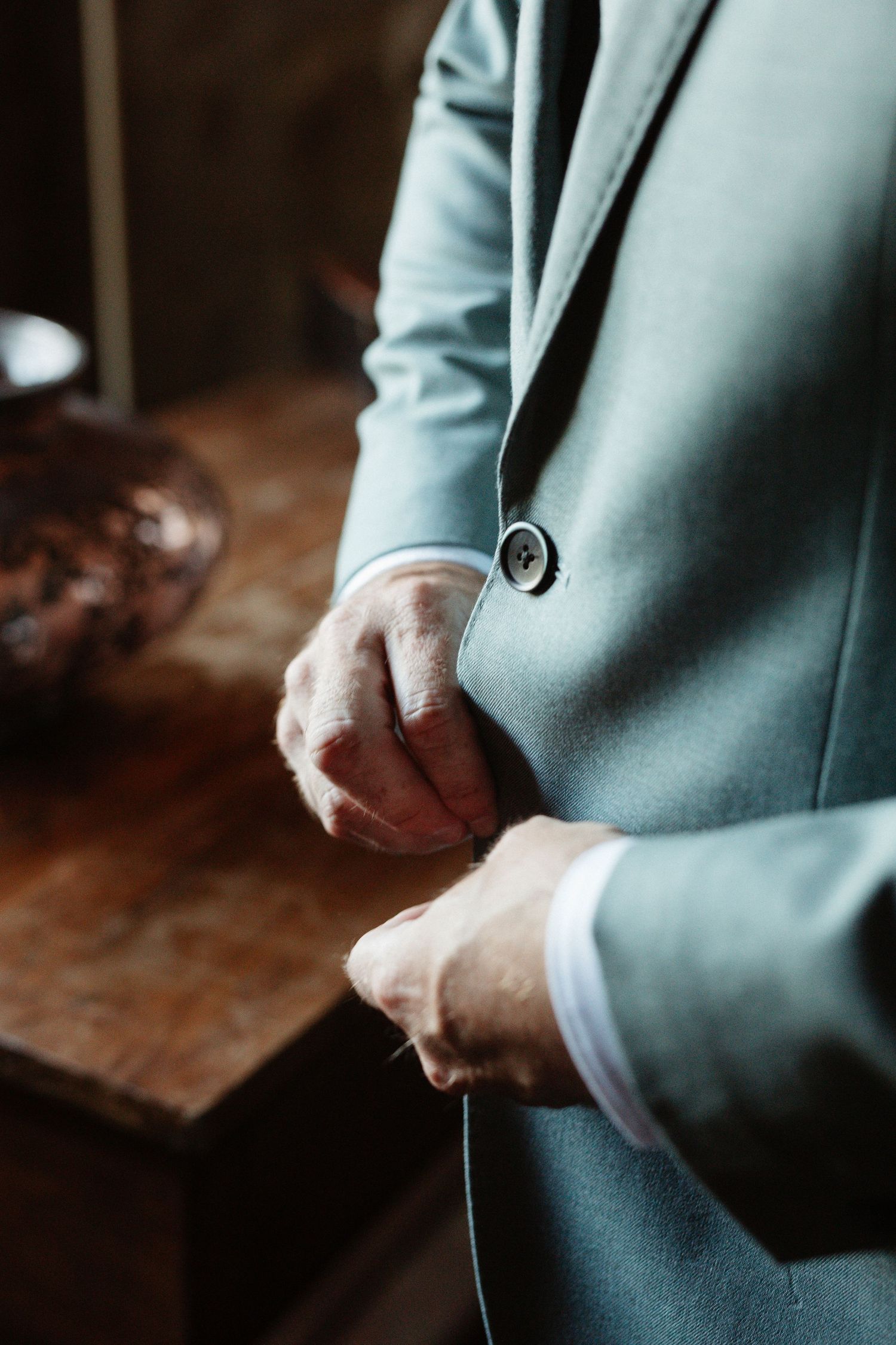 Man in light blue suit buttoning jacket, close-up of hands fastening button on elegant formal blazer.