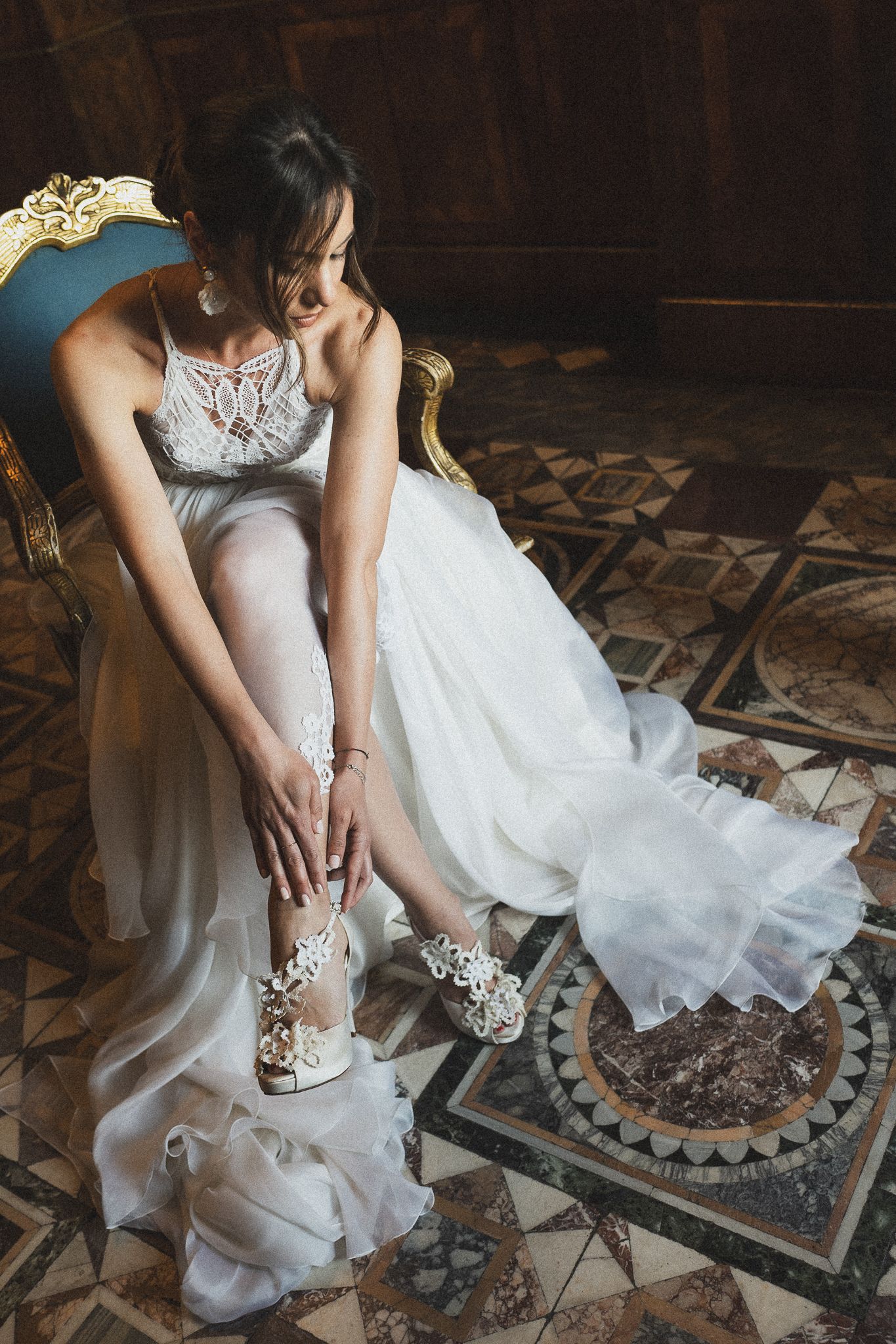 Wedding dress detail showing intricate lace shoes and flowing white fabric on ornate floor.