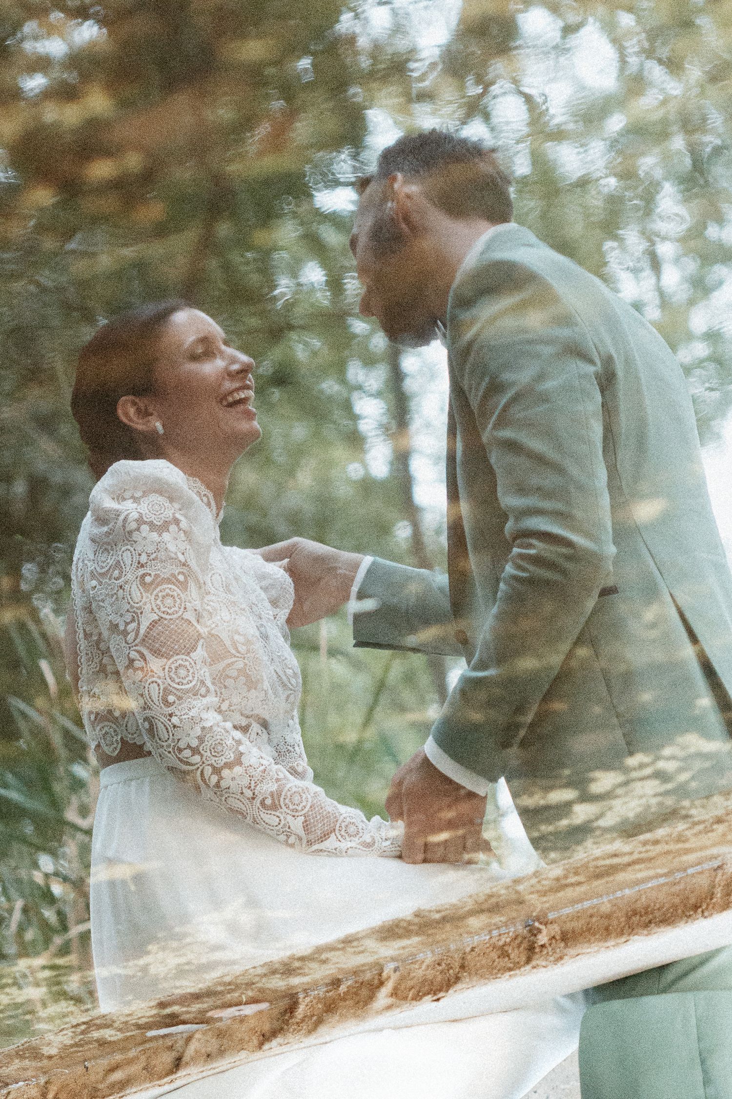 Candid moment of newlyweds sharing laughter outdoors in a dreamy forest setting.