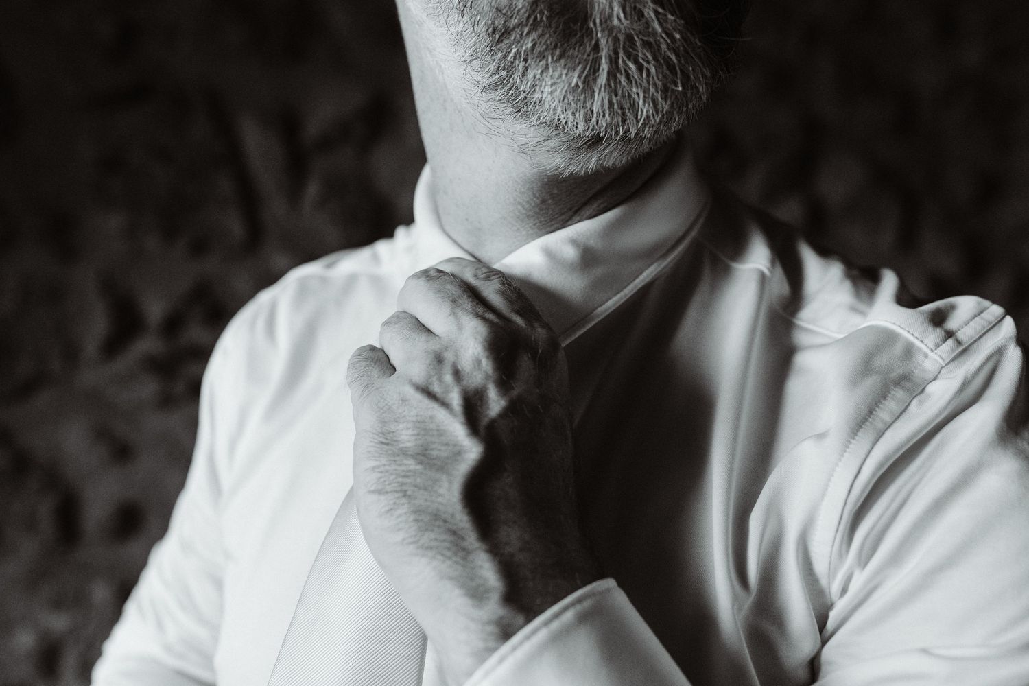 Black and white photo of a man in a white dress shirt adjusting his tie, elegant formal dressing concept.