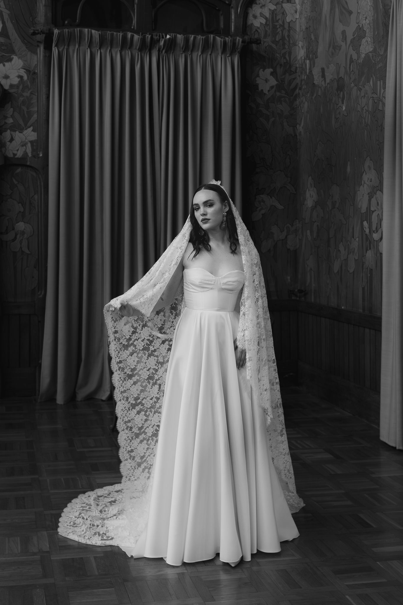 Elegant bride in a classic white wedding gown with sweetheart neckline and dramatic lace veil poses in black and white.