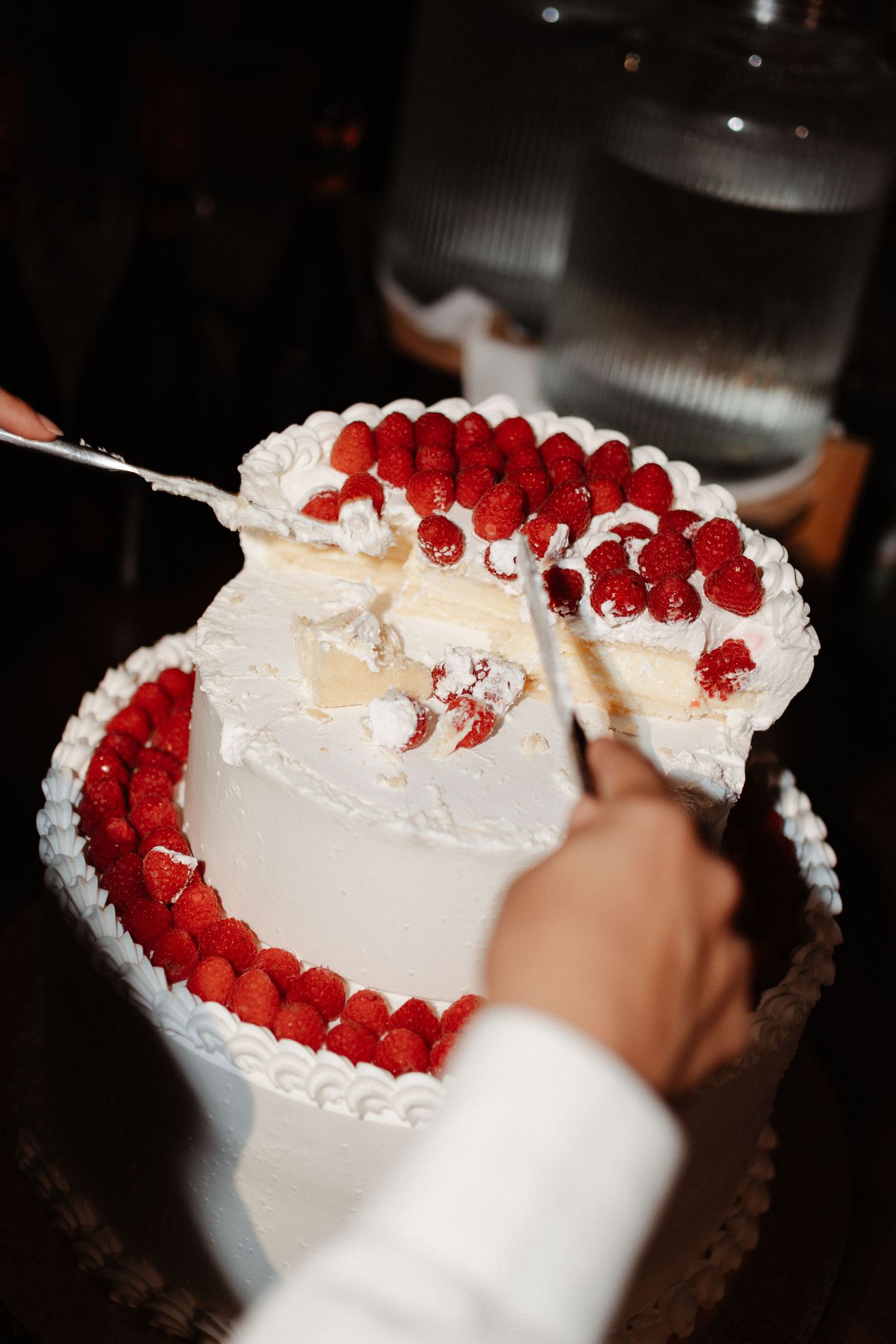 Heart-shaped wedding cake with white frosting and fresh raspberries being sliced at a celebration.