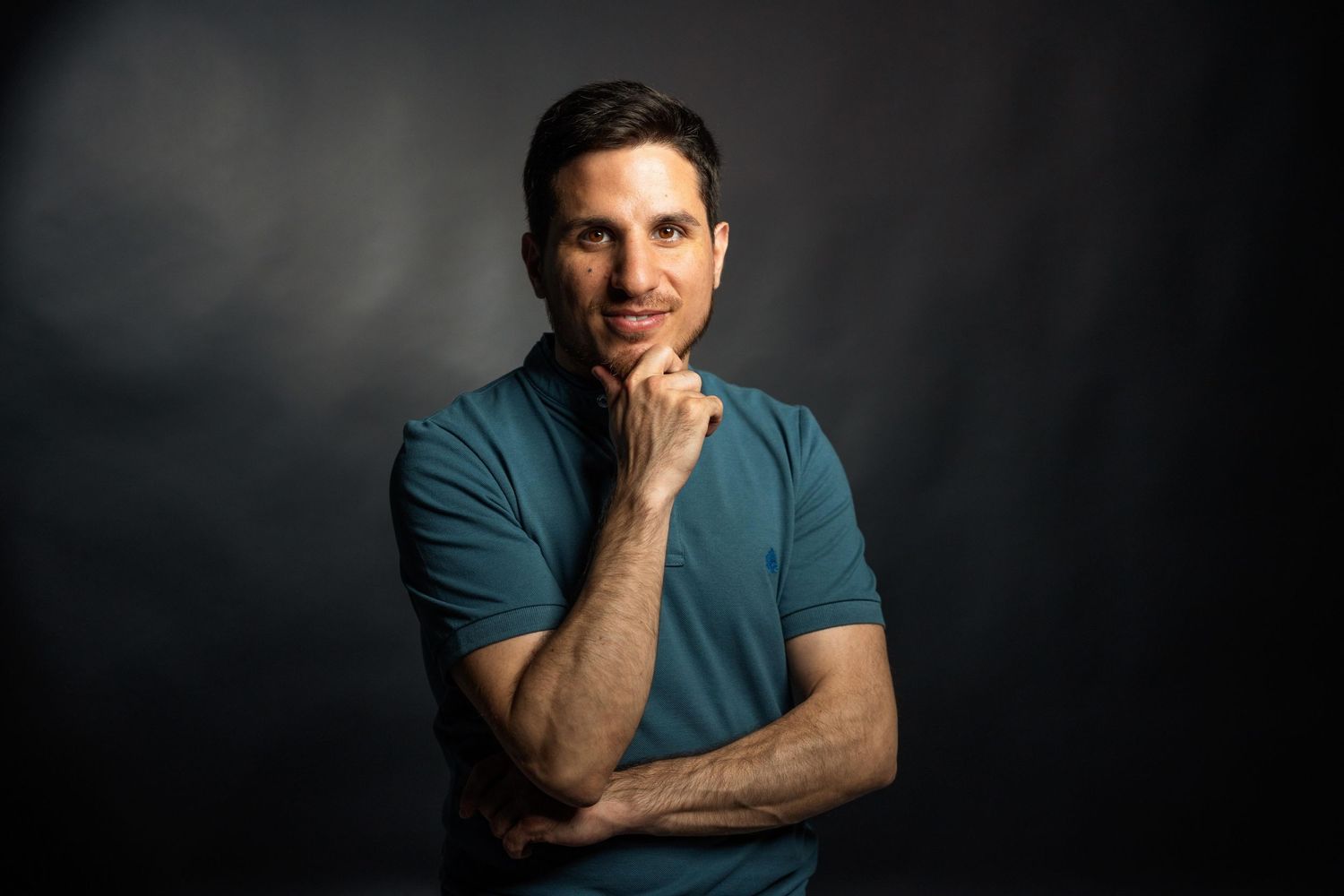 Portrait of man in teal shirt against dark background with contemplative expression.