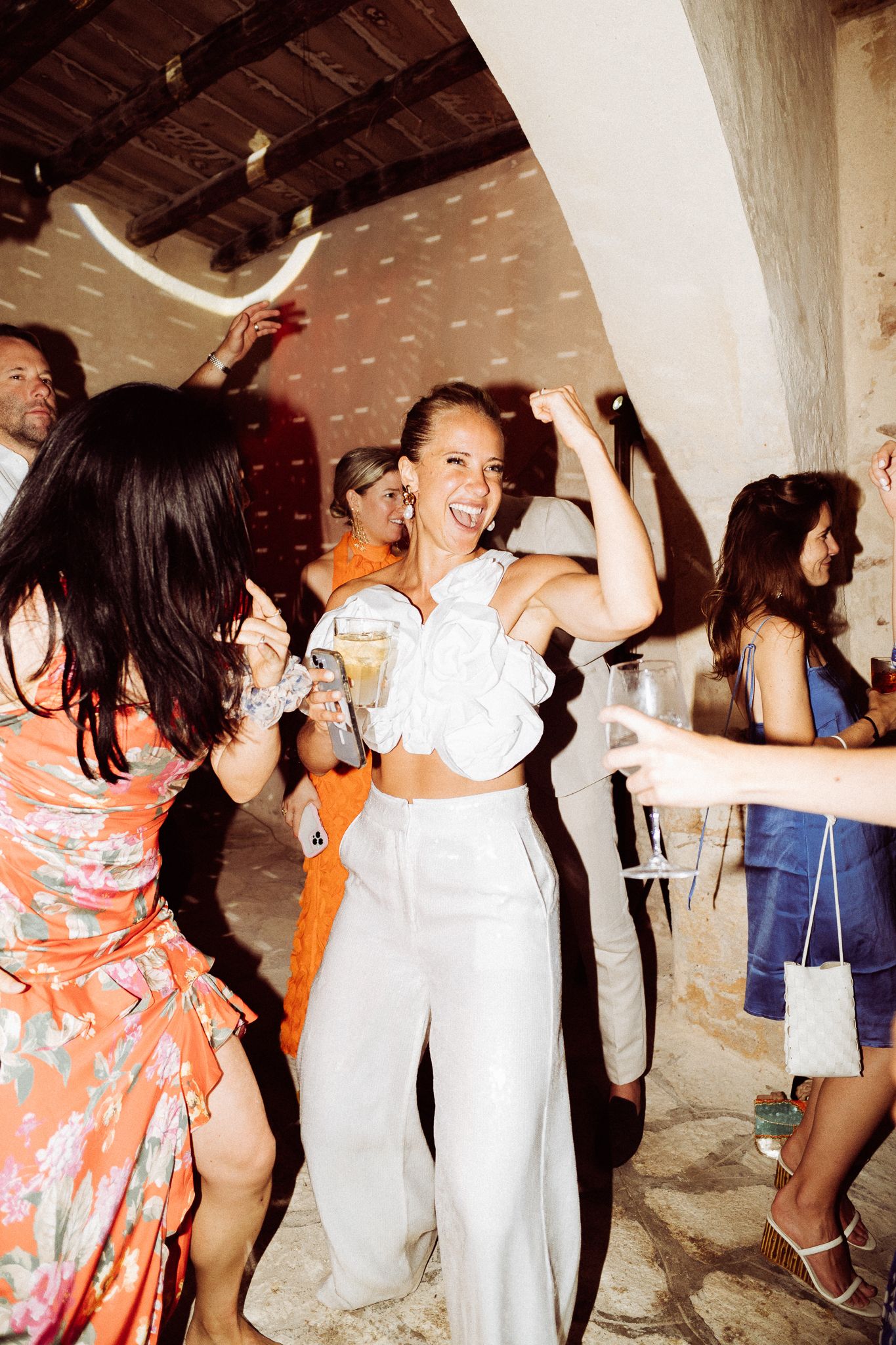 Wedding reception guests dancing and celebrating with joyful energy under rustic ceiling.