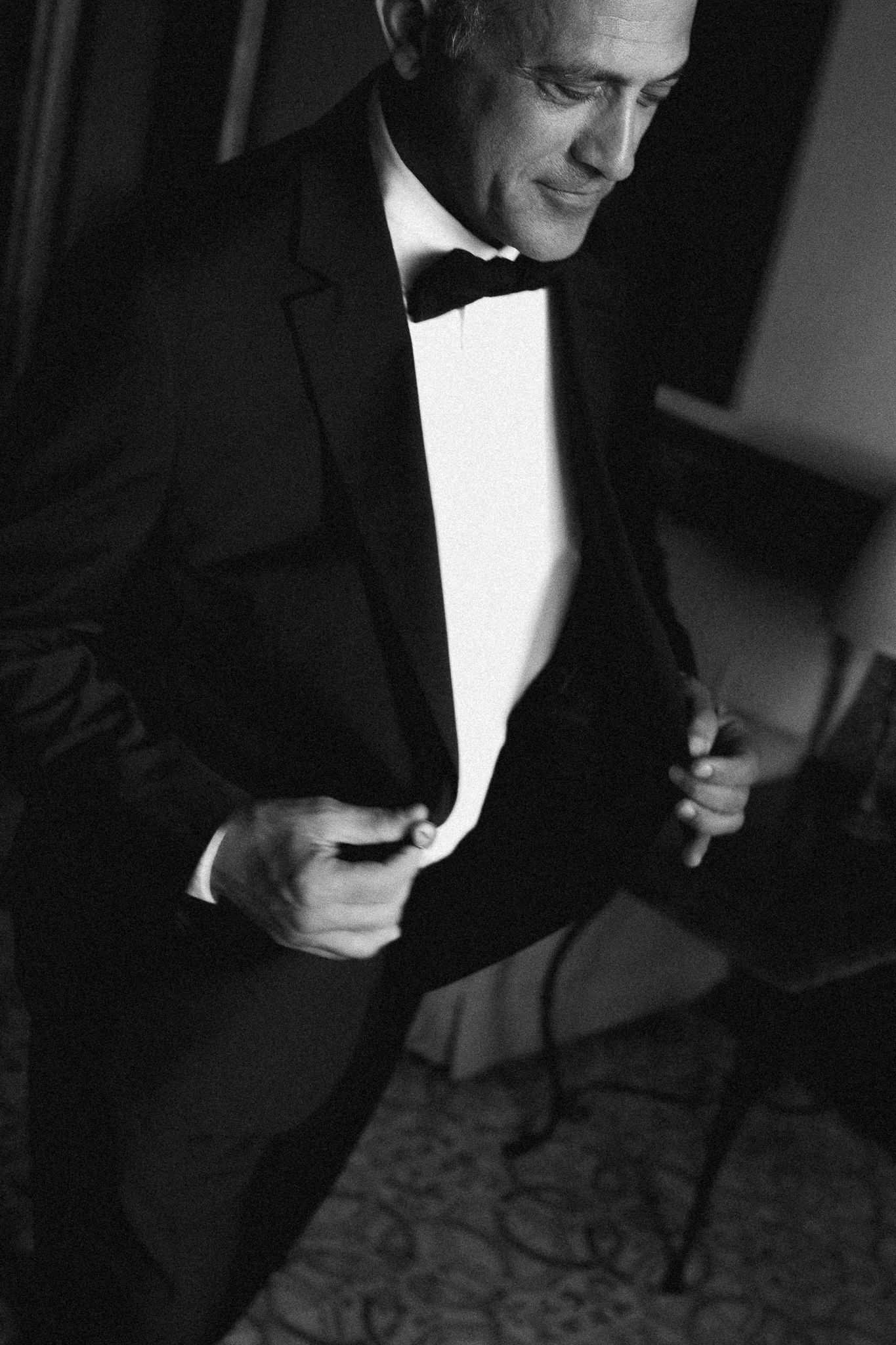 Classic black and white portrait of person adjusting bowtie in formal attire. Sicily wedding. Palermo. Siracusa. Scopello.