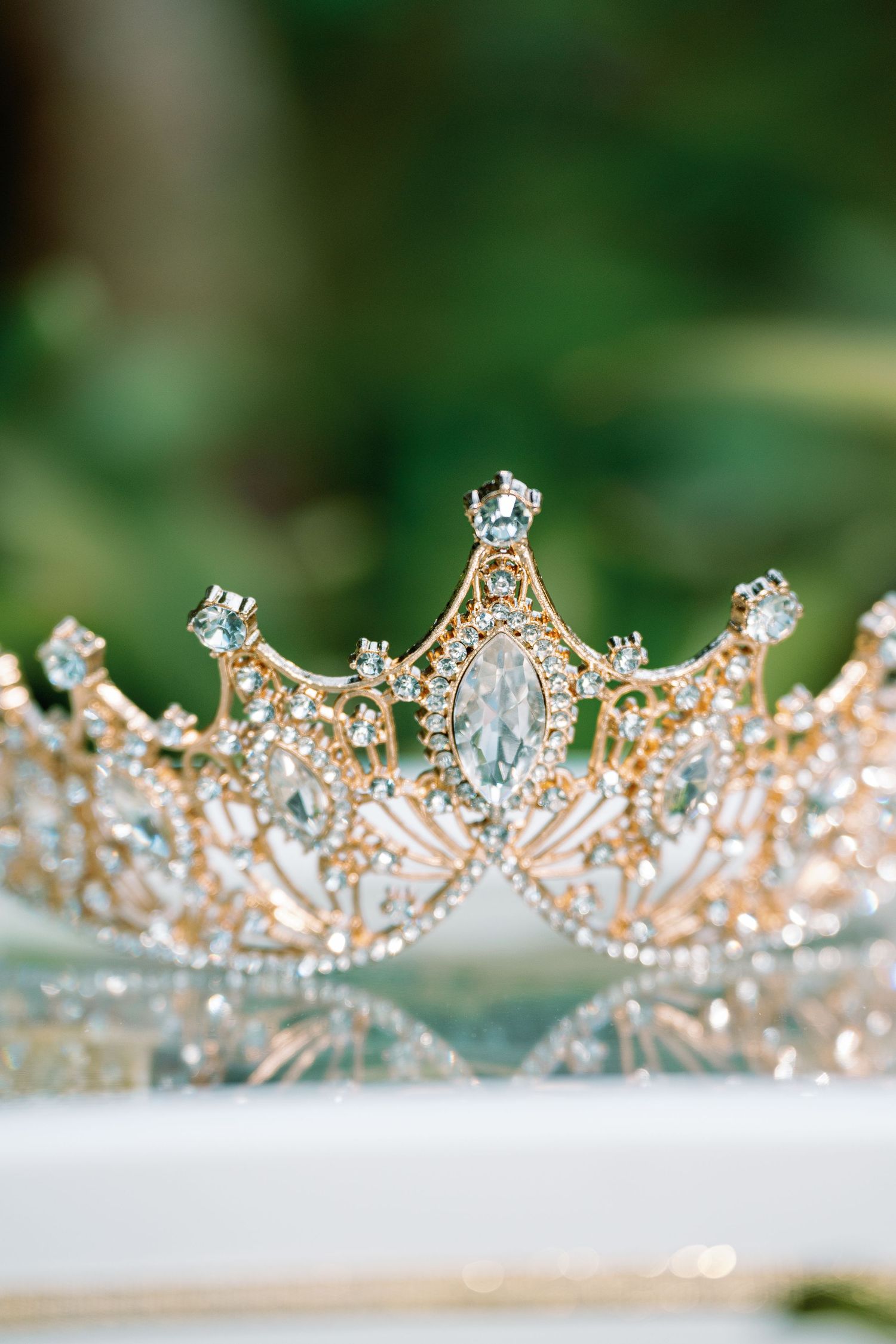 Delicate rose gold tiara with crystal embellishments displayed against a blurred green background.