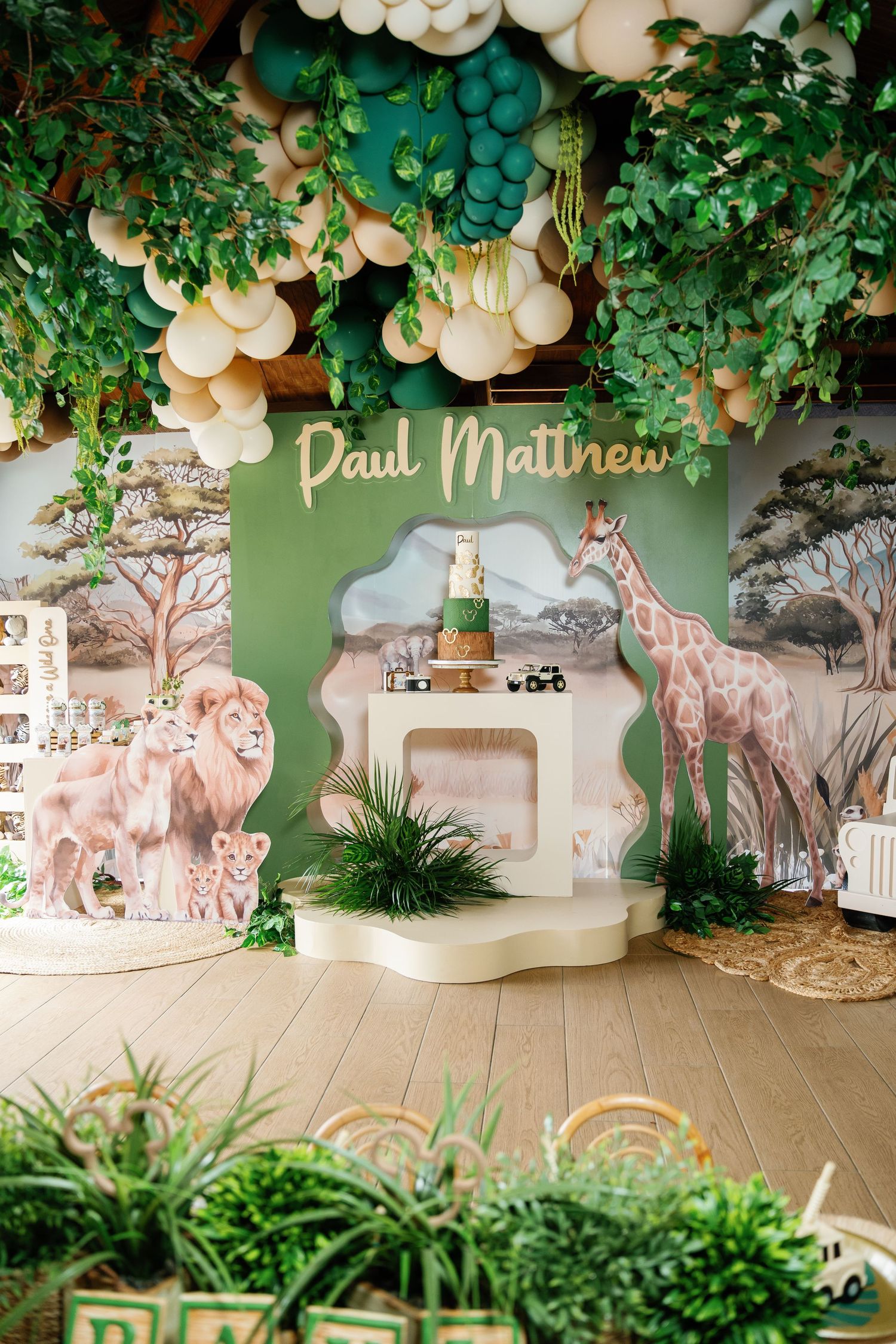 Safari-themed party backdrop with balloon arch, greenery, and custom name signage.
