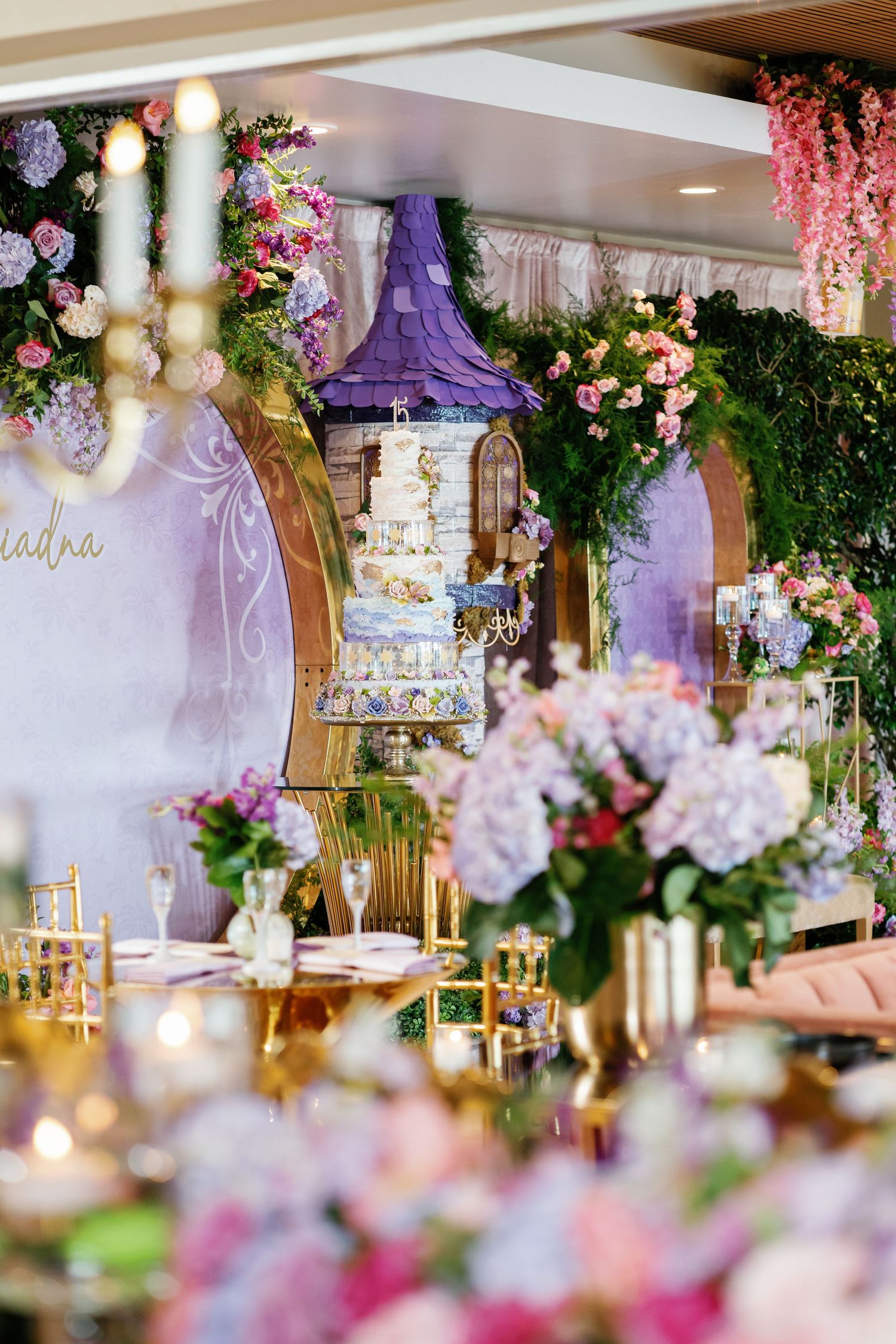 Enchanted garden themed party with purple tower centerpiece, floral arrangements, and hanging pink flowers.