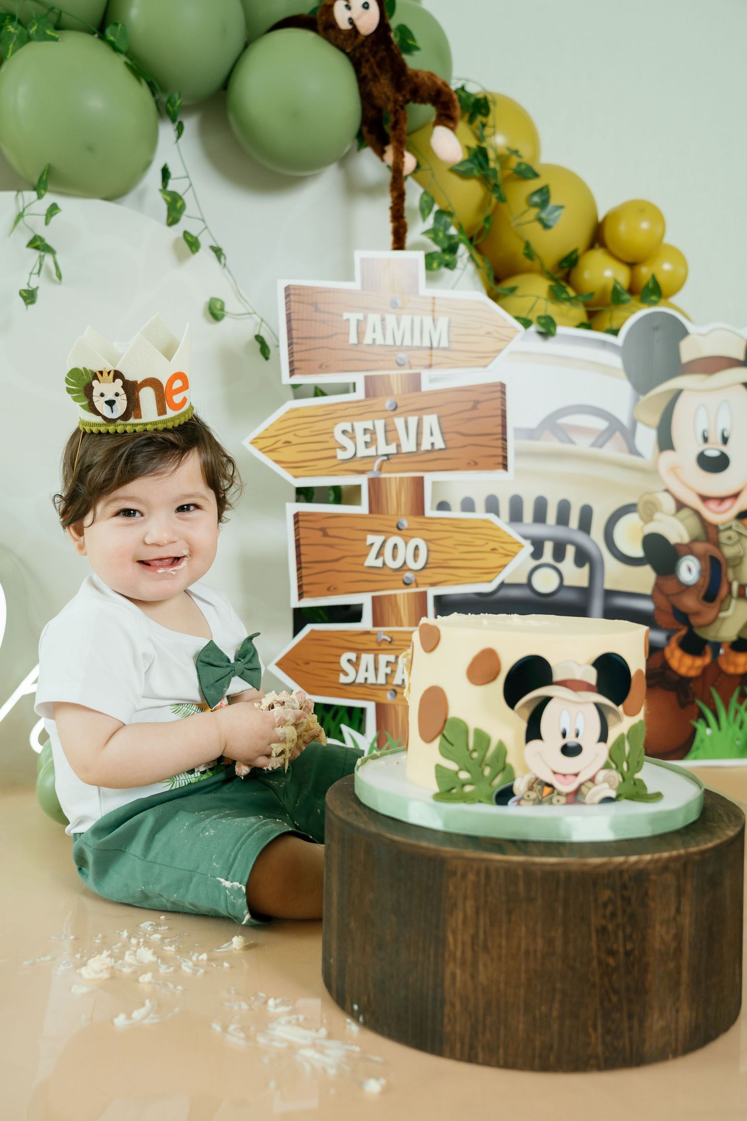 Safari-themed birthday party setup with wooden signs, green balloons, and jungle animal decorations.
