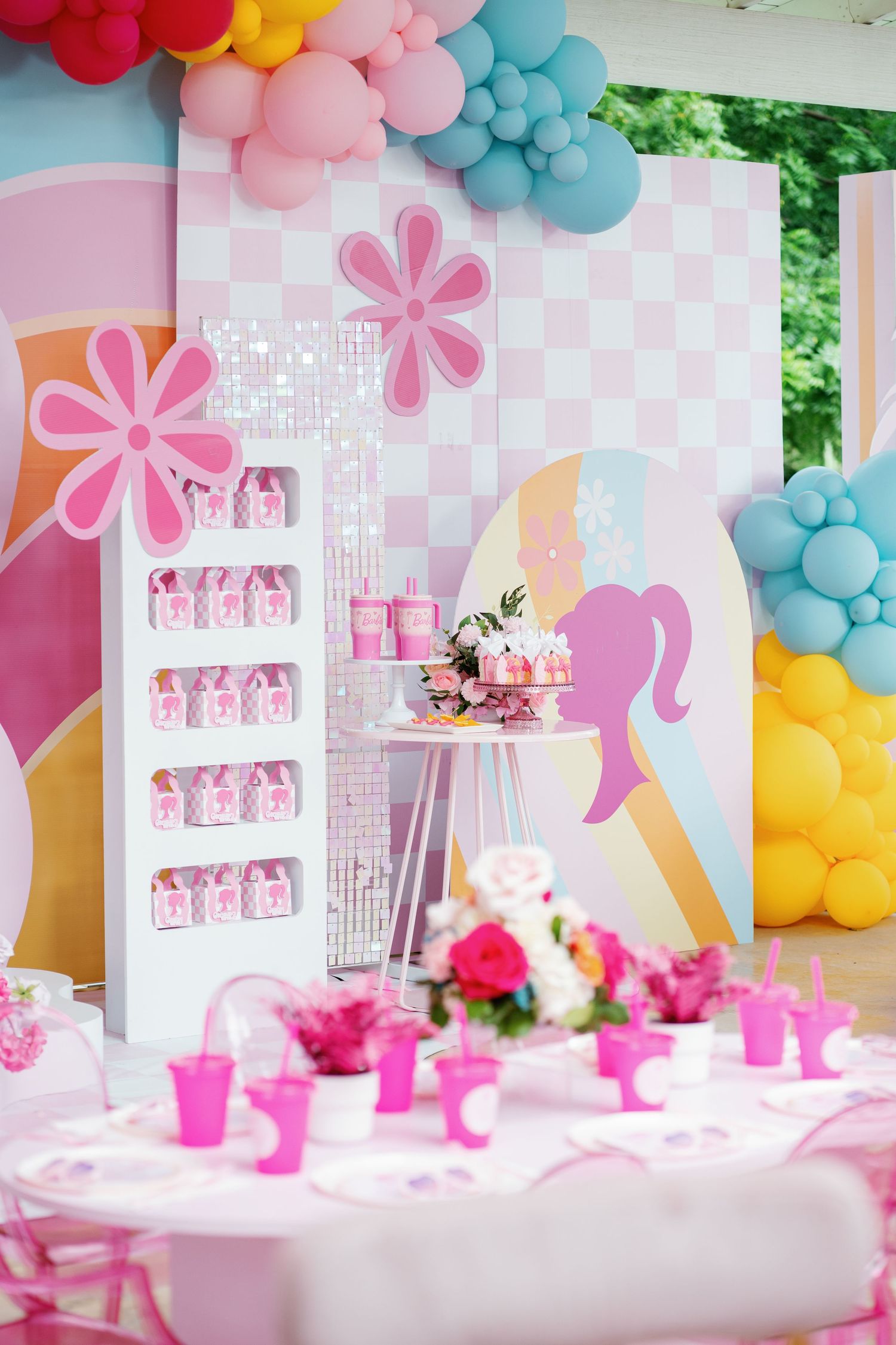 Colorful party setup with pink and blue balloons, checkered backdrop, and bow decorations.