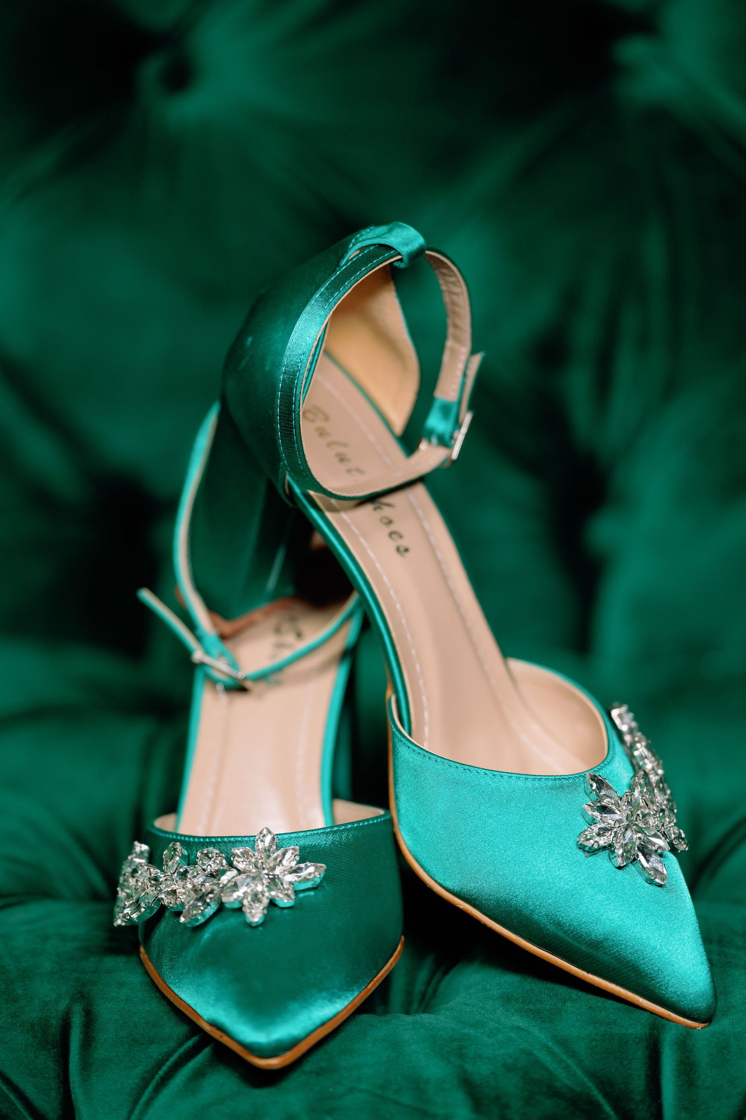 Teal satin heels adorned with crystal butterfly embellishments against a dark background.