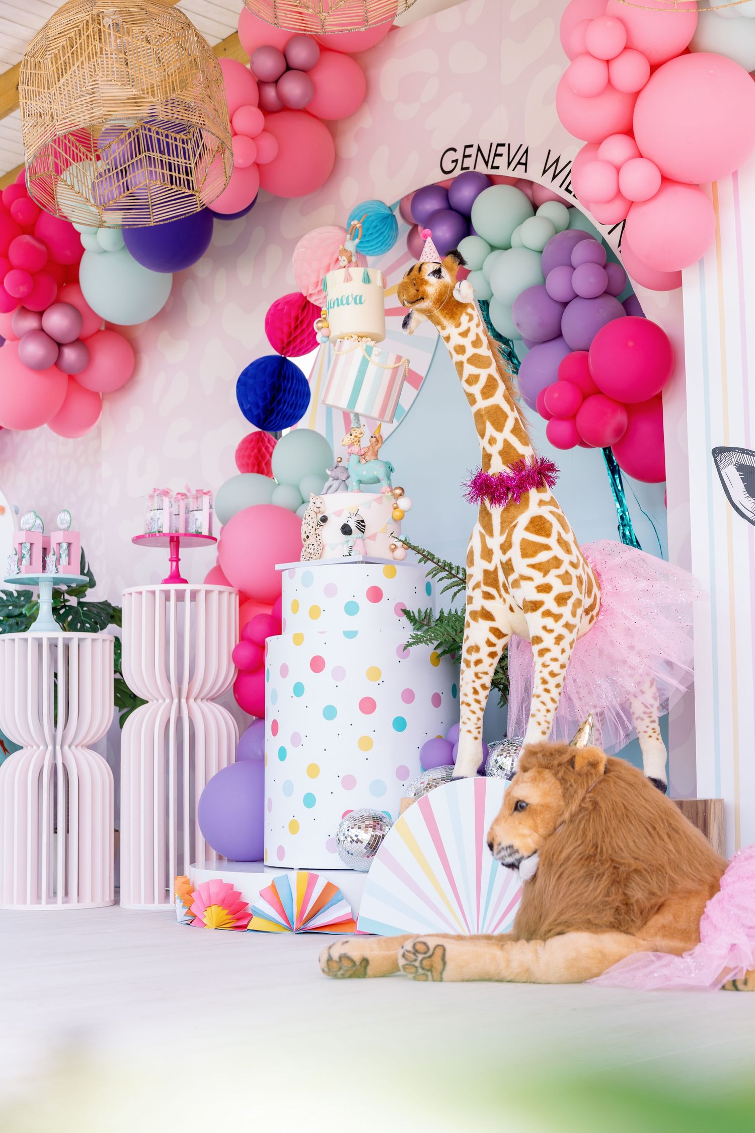 Safari themed party decor with pink balloons, giraffe plush toys, and striped gift boxes.