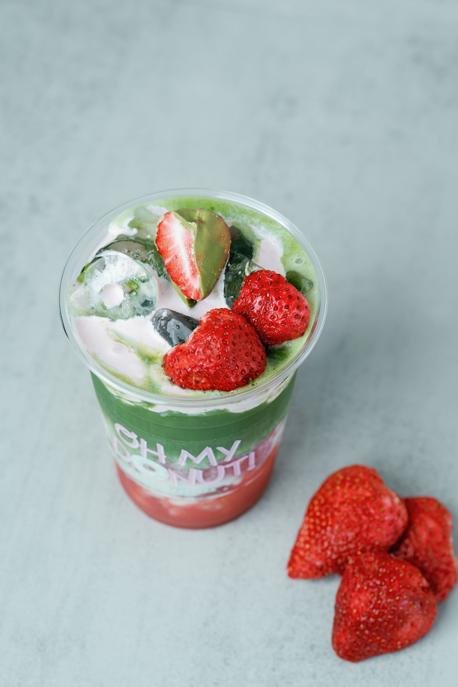 Fresh strawberry yogurt parfait with whipped cream in a clear plastic cup on a light gray background.