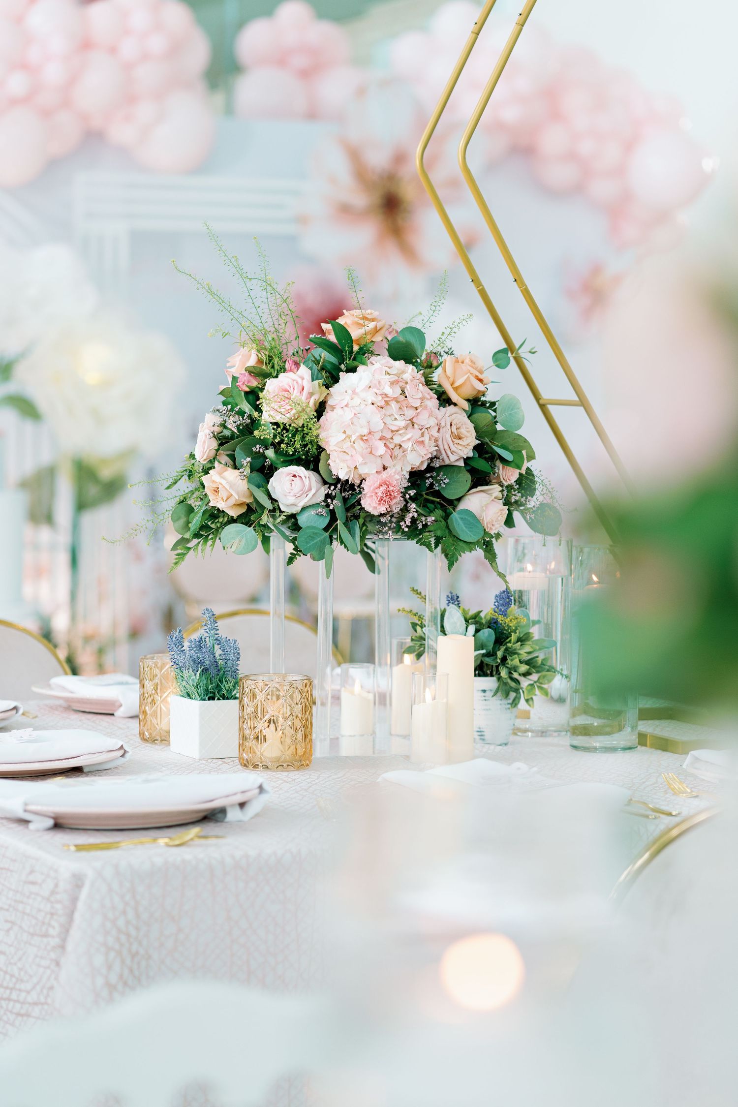 Elegant table setting with pink floral centerpieces and gold accents under soft lighting.