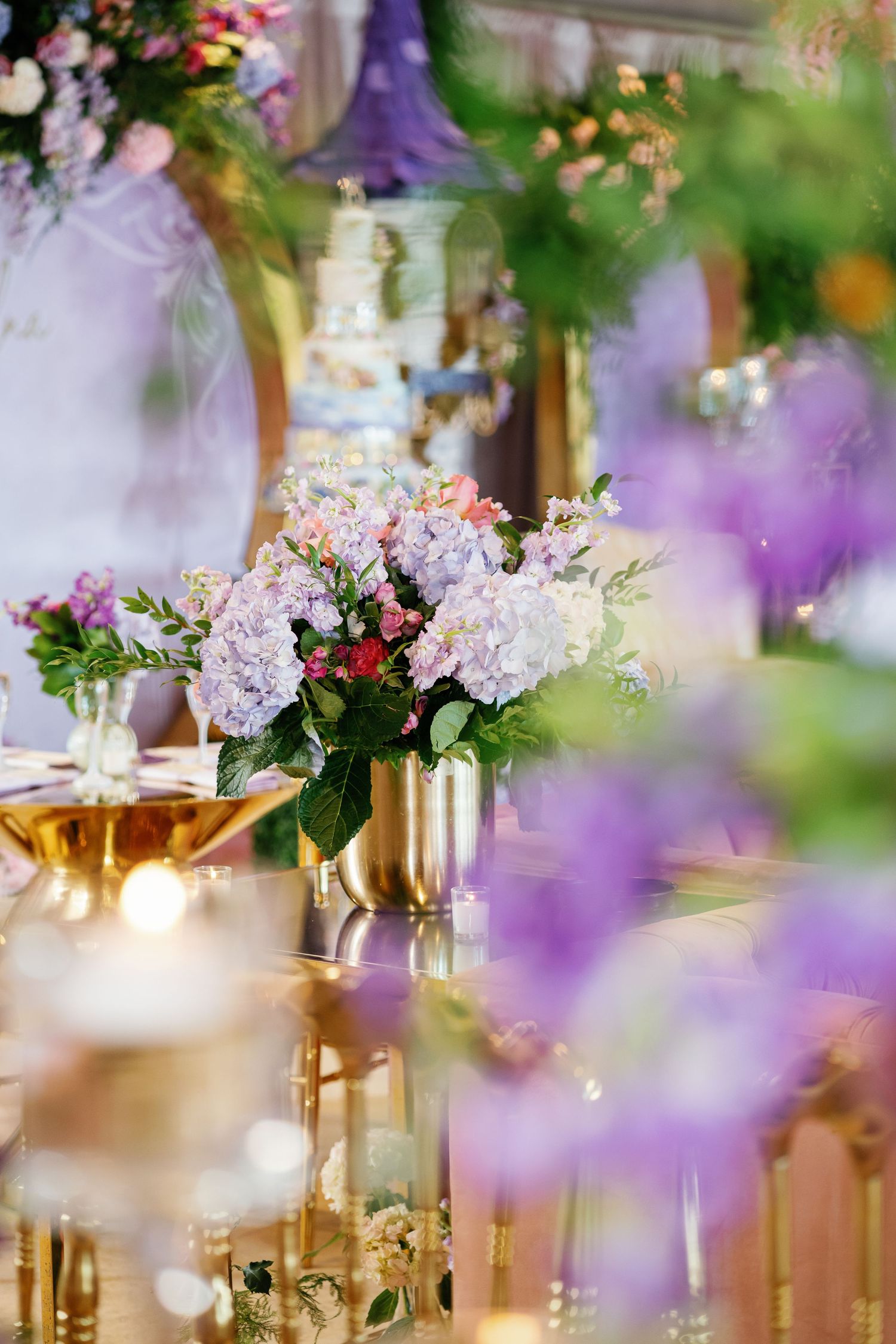 Ethereal wedding reception decor with pink flowers, gold vases, and soft purple lighting.
