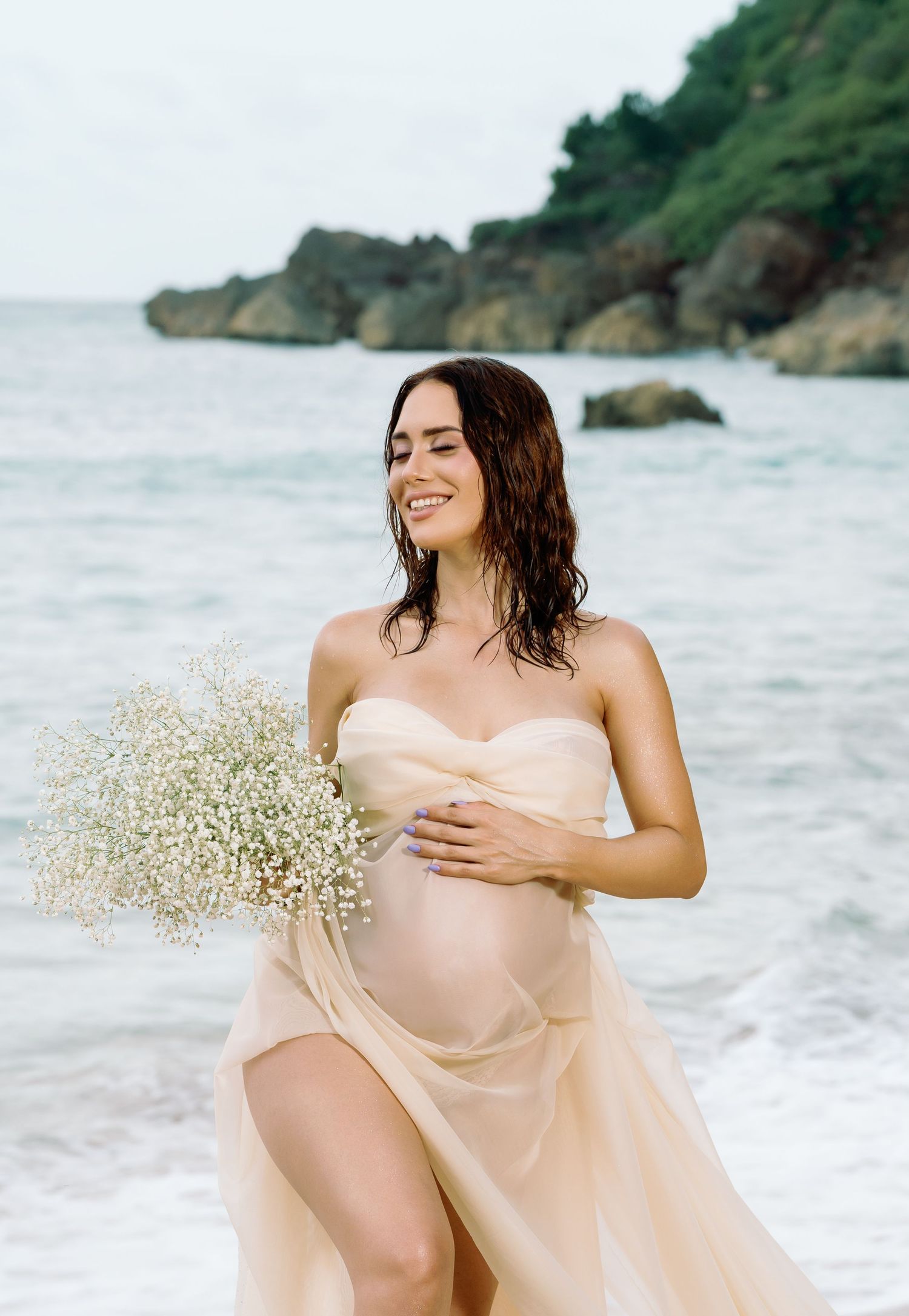 Romantic beach maternity photos with flowing sheer dress and baby's breath flowers.