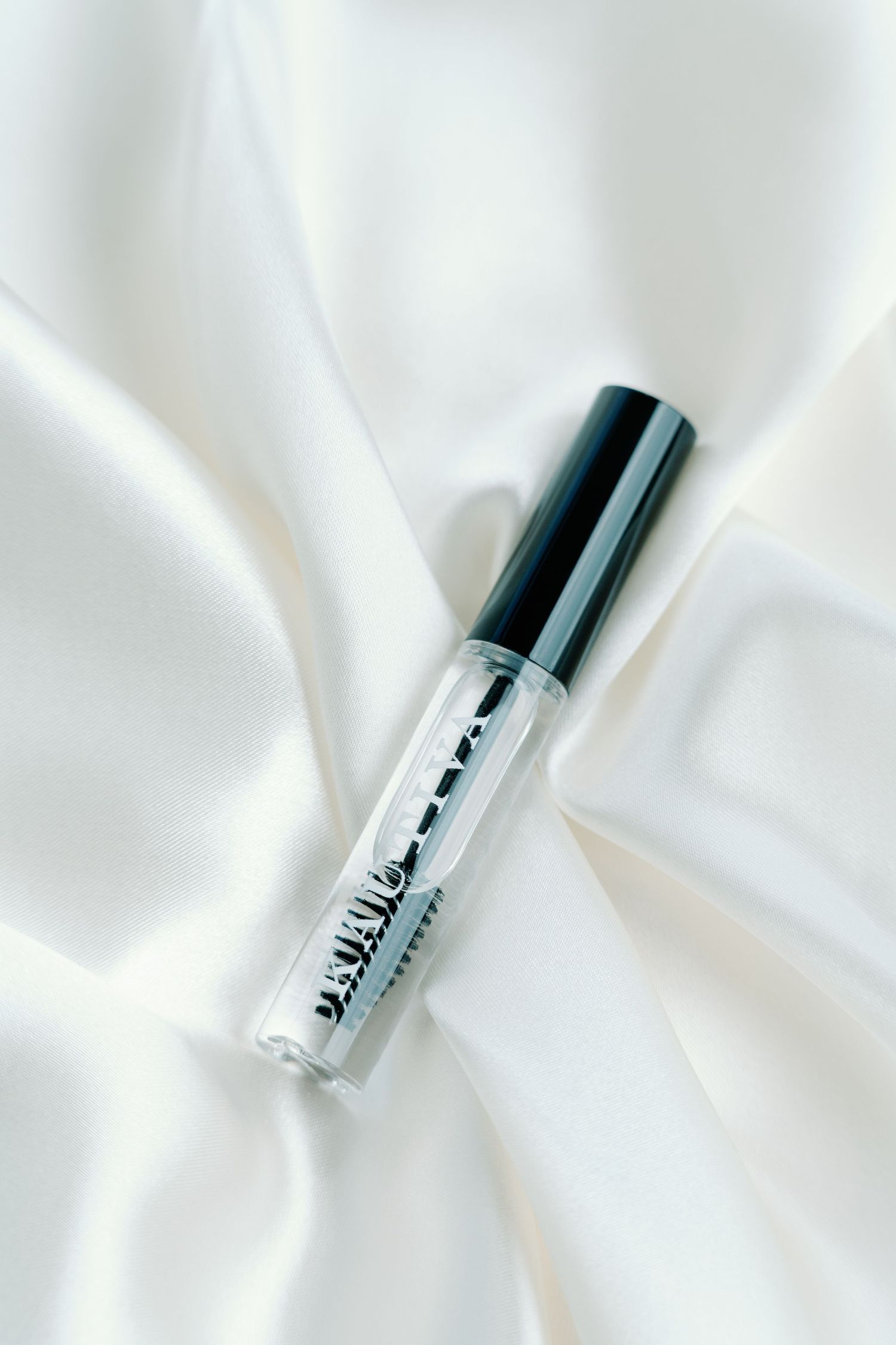 Clear cosmetic bottles arranged diagonally on white silk fabric.