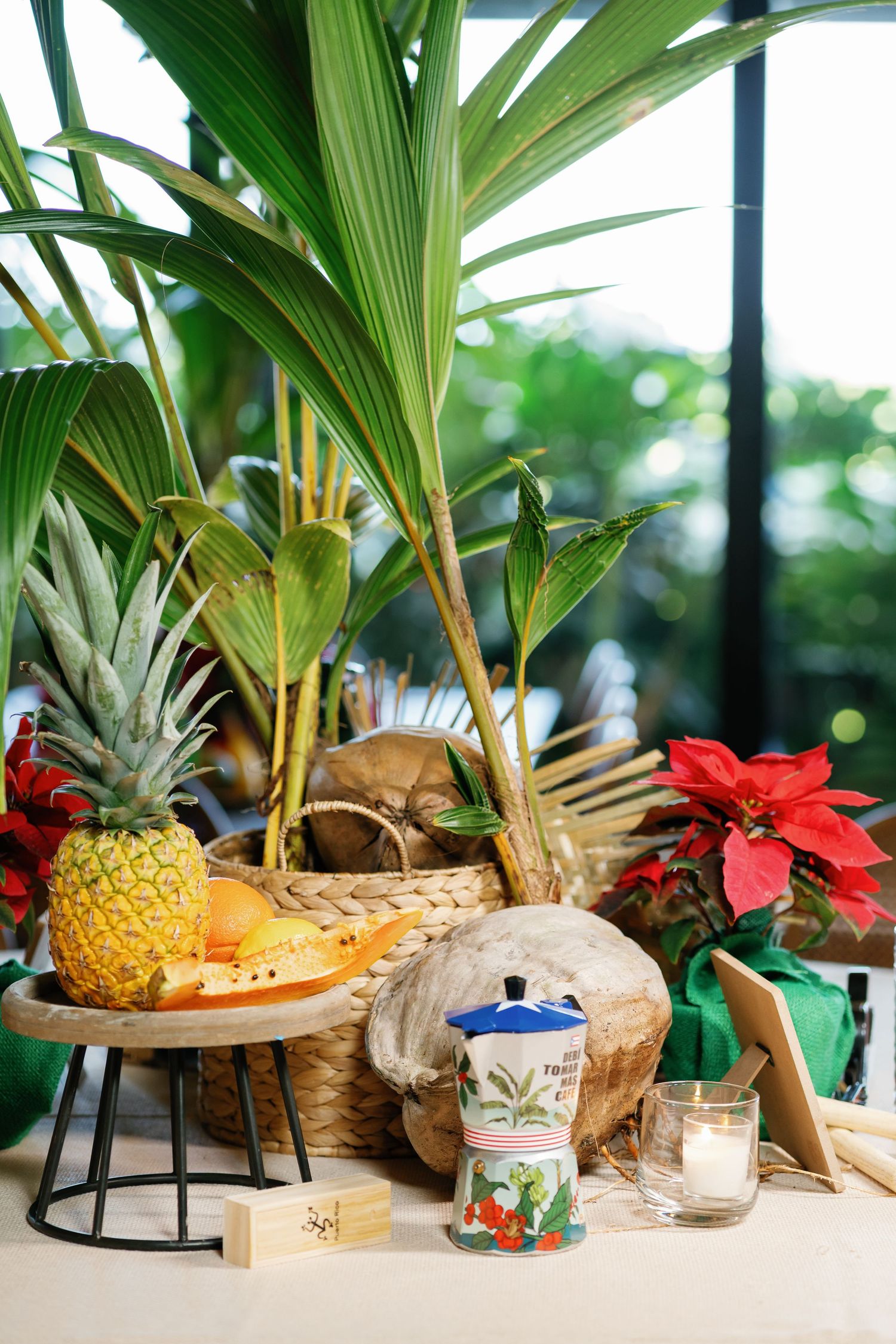 Tropical themed party decor with palm leaves, pineapples, and red flowers arranged on wooden tables.