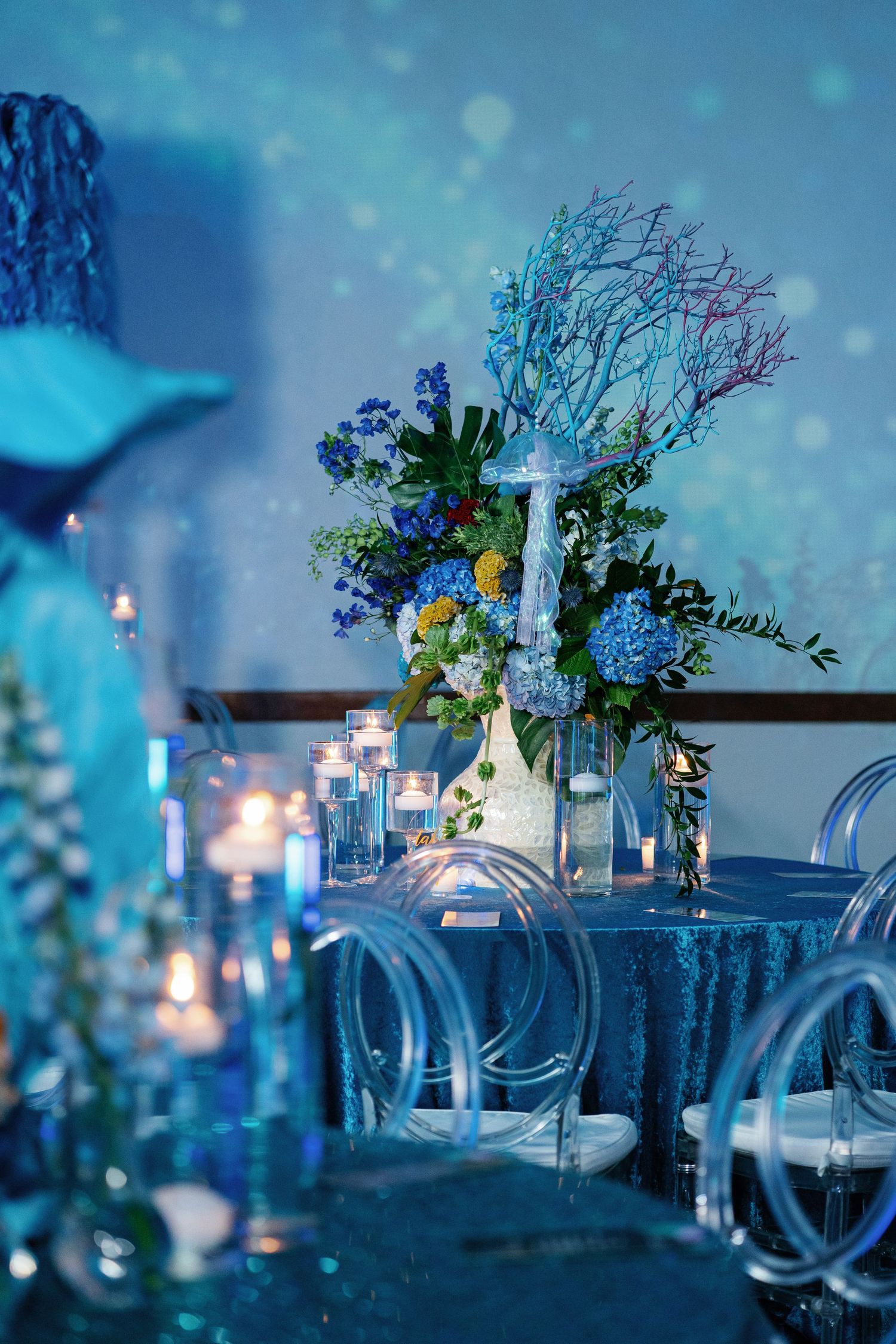 Elegant blue-tinted wedding reception decor with floral centerpieces and candlelight.