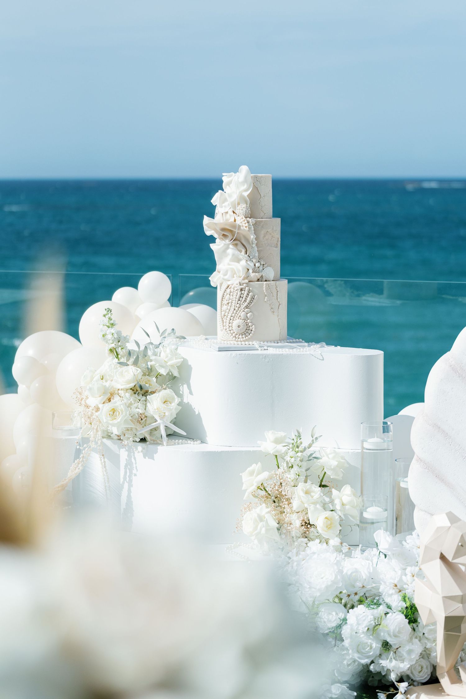 Elegant beach wedding decor featuring white floral arrangements and candles against a turquoise ocean backdrop.