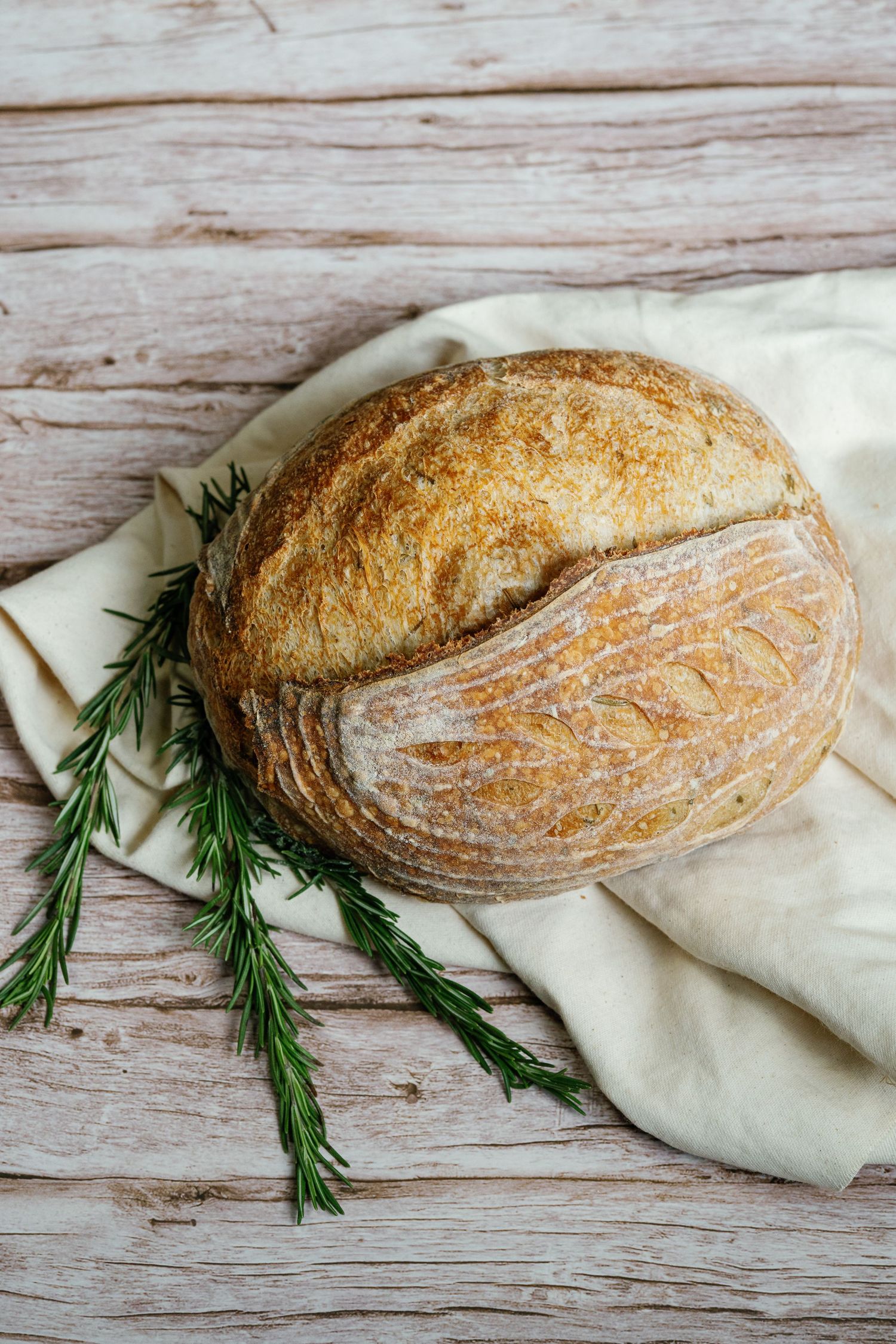 Artisanal sourdough bread loaf with fresh rosemary sprigs on rustic wooden background.