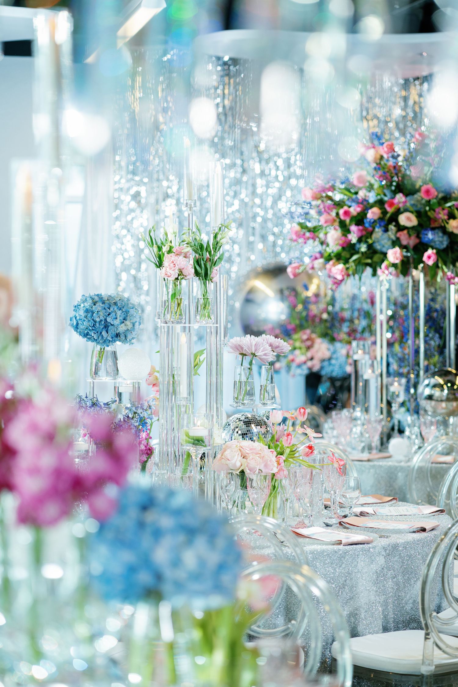 Modern wedding reception decor featuring crystal vases, colorful floral arrangements, and silver tablescapes.