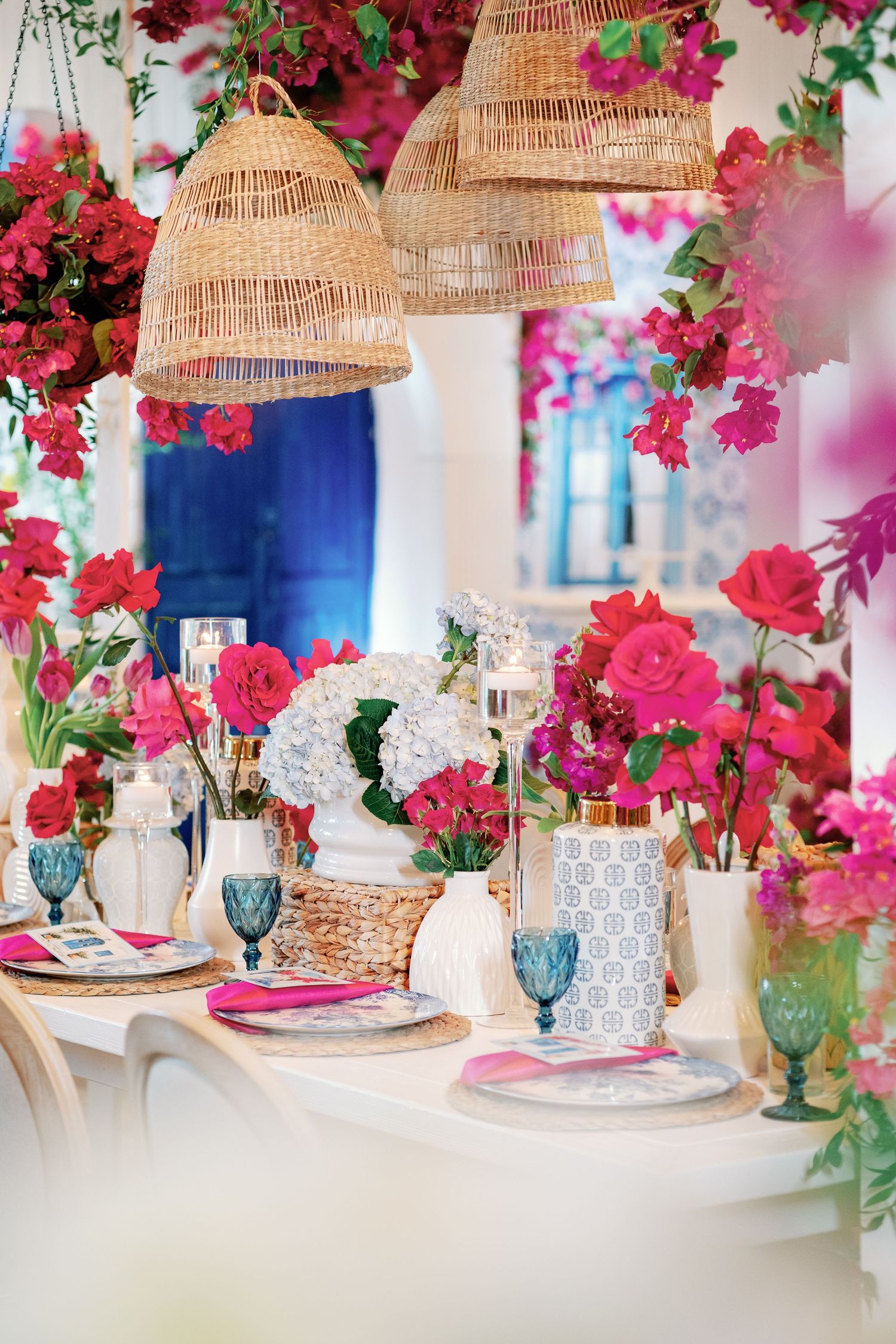 Tropical-inspired table setting with woven pendant lamps, bright bougainvillea flowers, and blue glassware.
