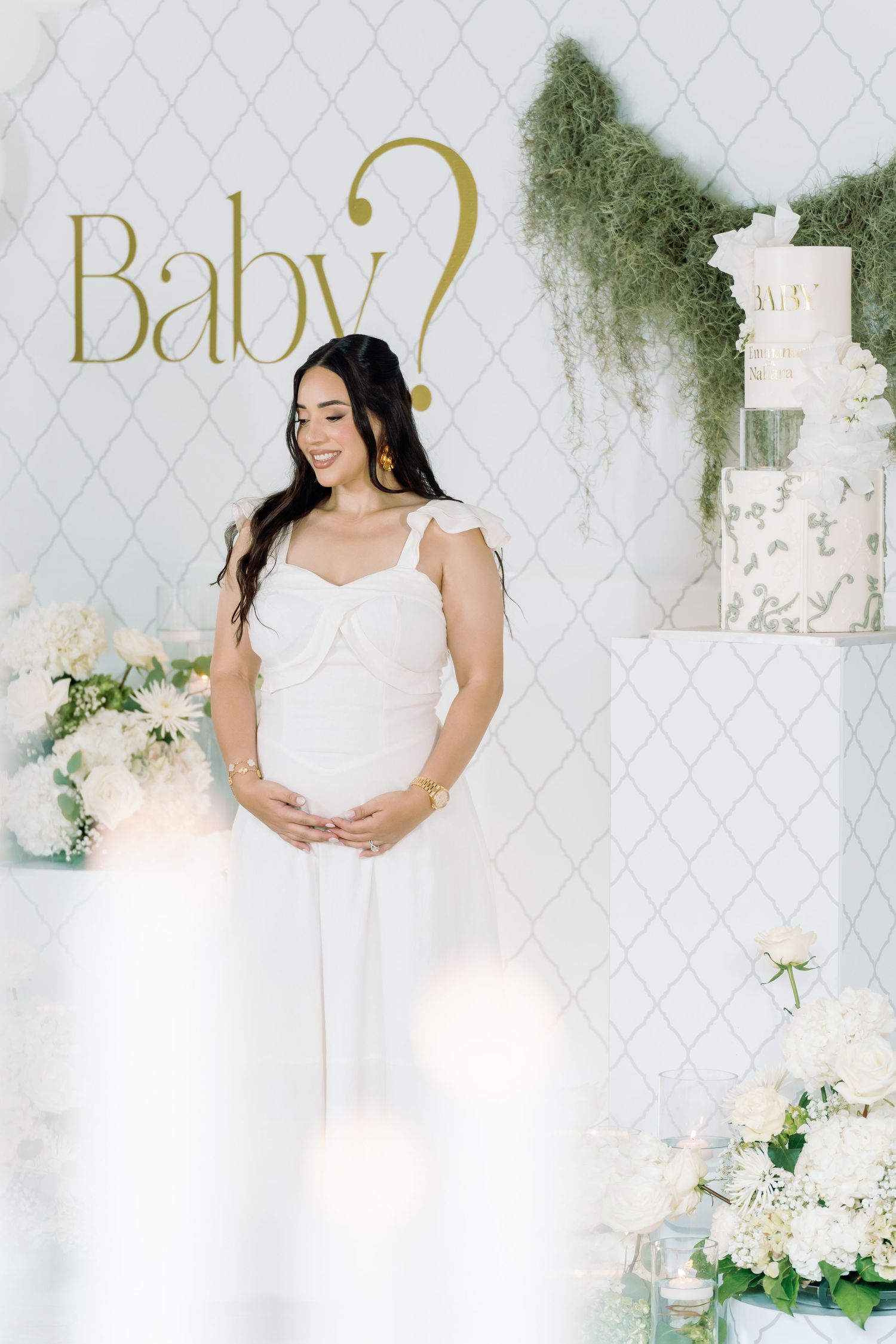 Maternity photoshoot setup with white lattice backdrop, floral arrangements and elegant gold lettering.