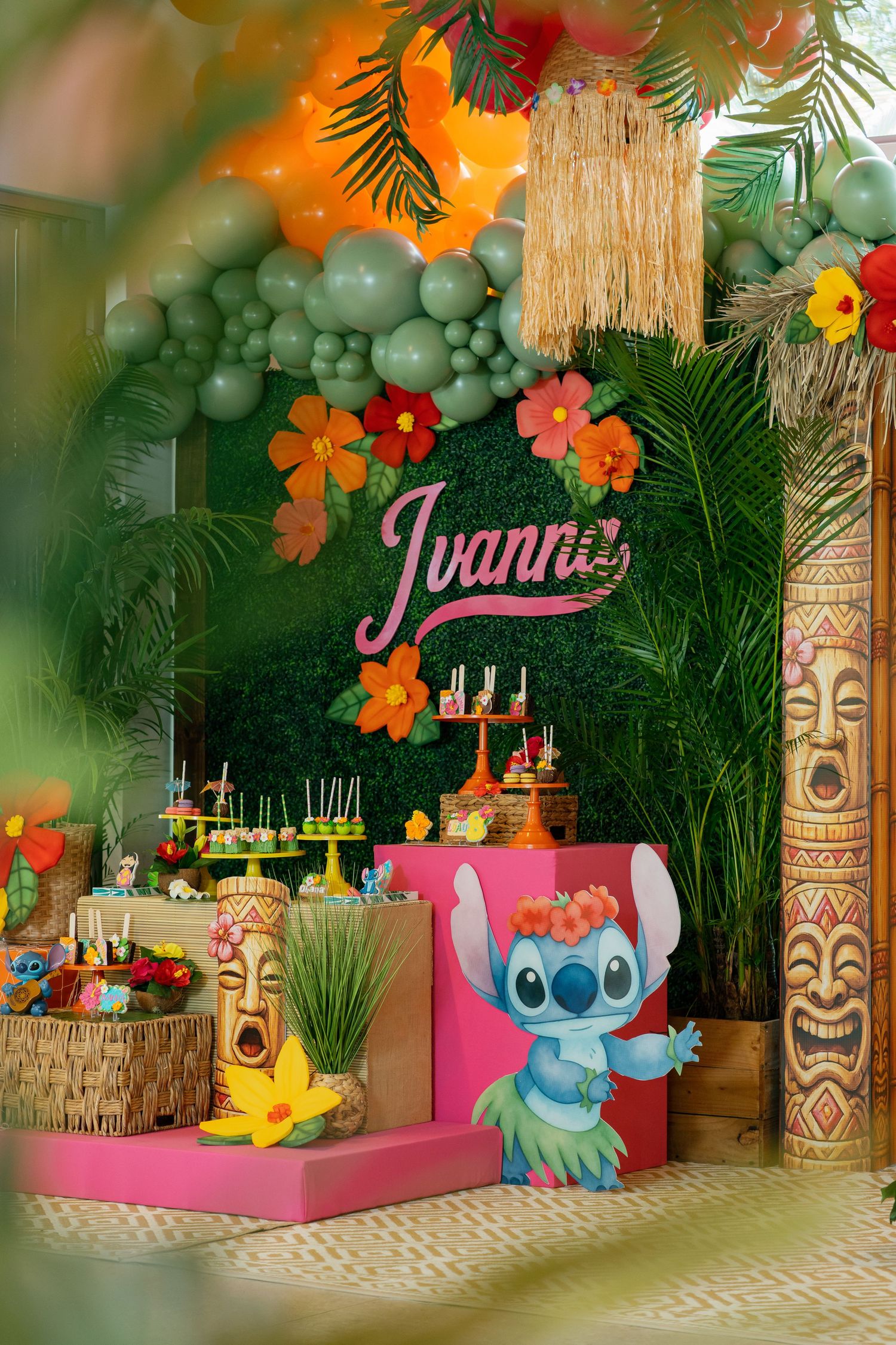 Lilo & Stitch themed birthday party setup with tropical decor, balloon arch, tiki statues, and Ivanna name sign.