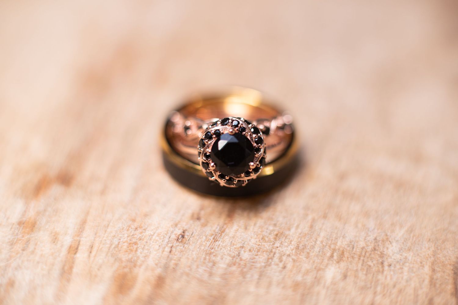 Rose gold engagement ring with black diamond center stone and halo setting displayed on wooden surface.