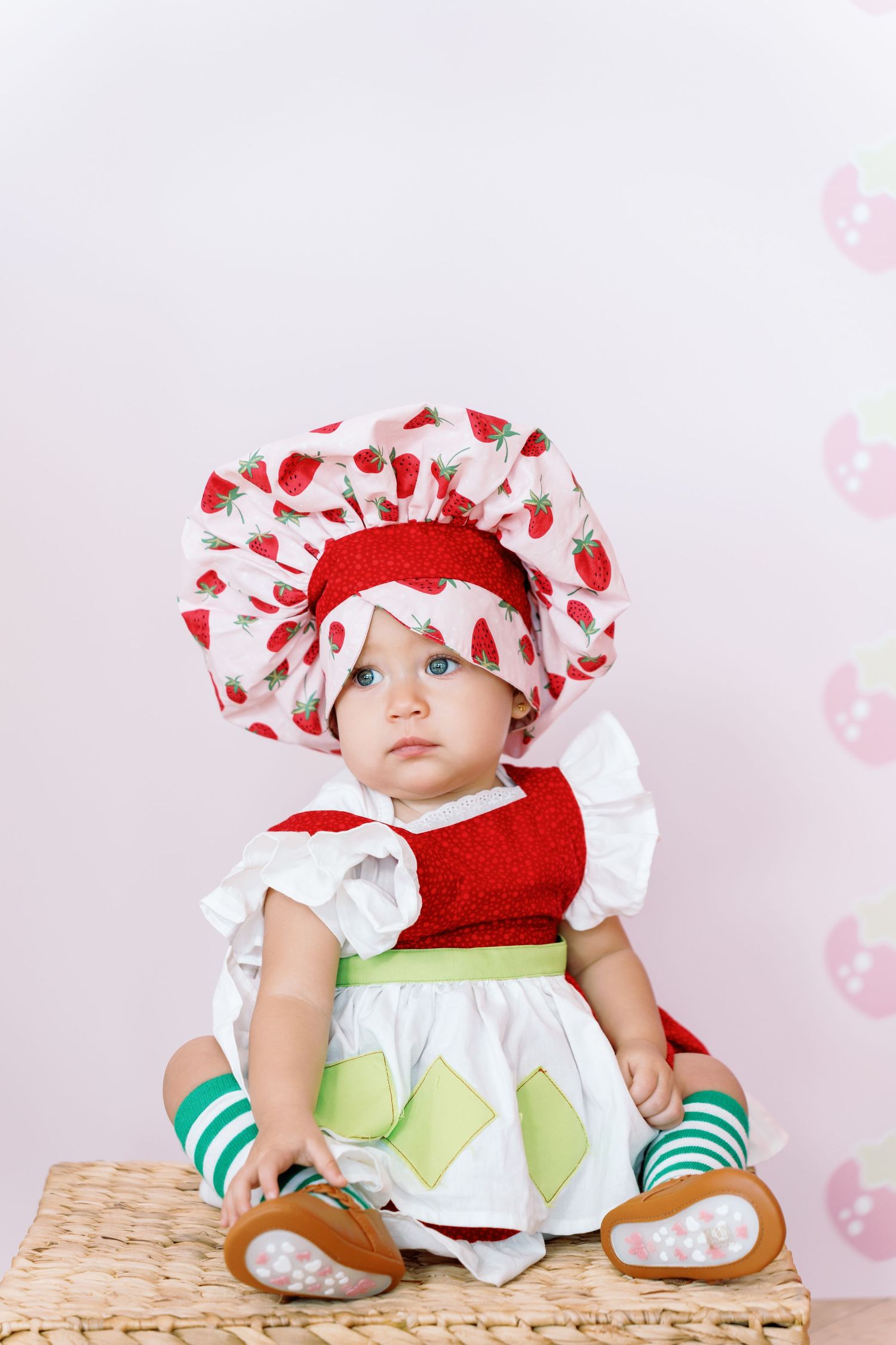 Baby wearing red and white strawberry-themed costume sitting on wooden surface.