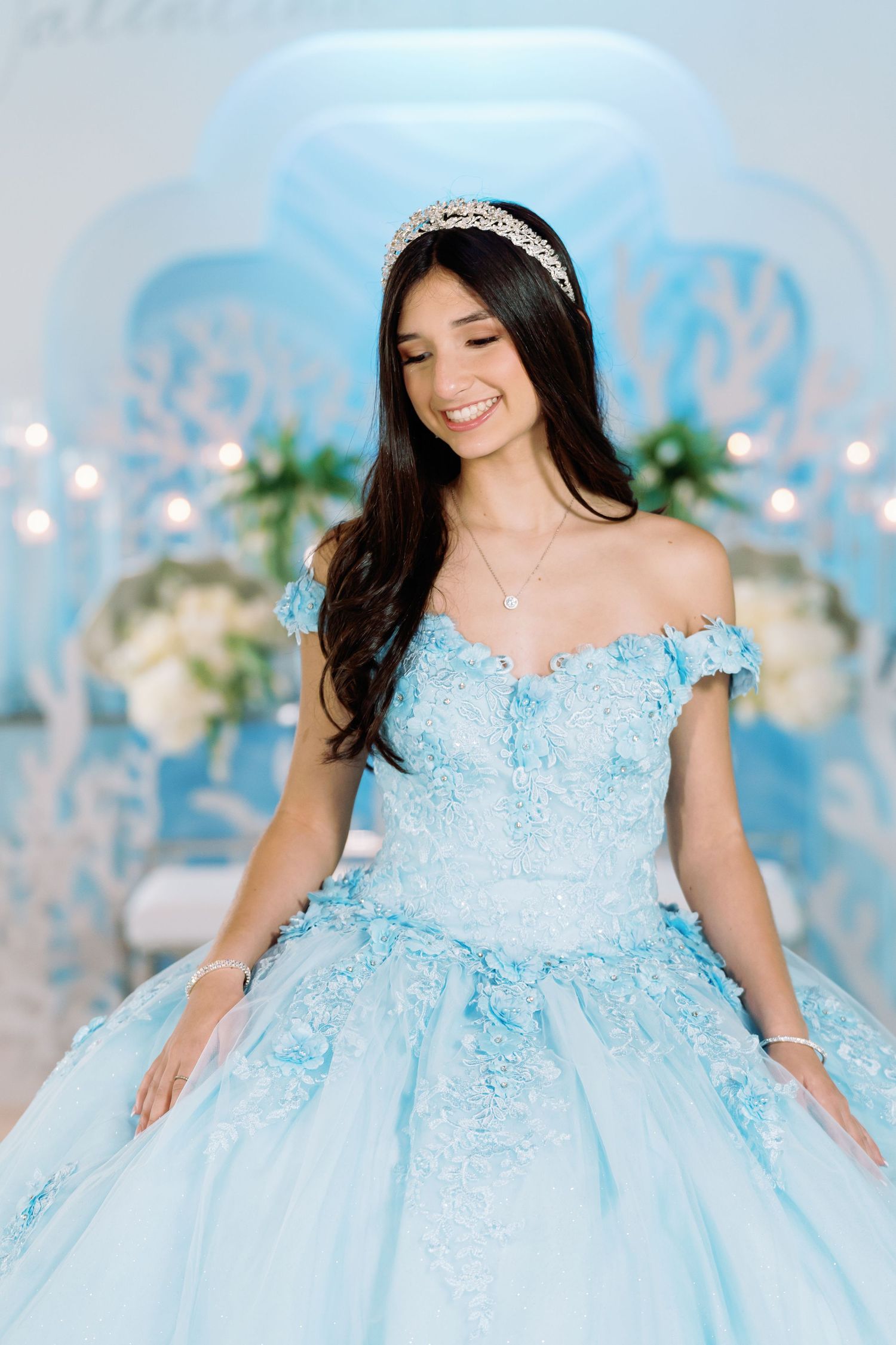 Elegant light blue ball gown with intricate lace details and off-shoulder design in a dreamy setting.