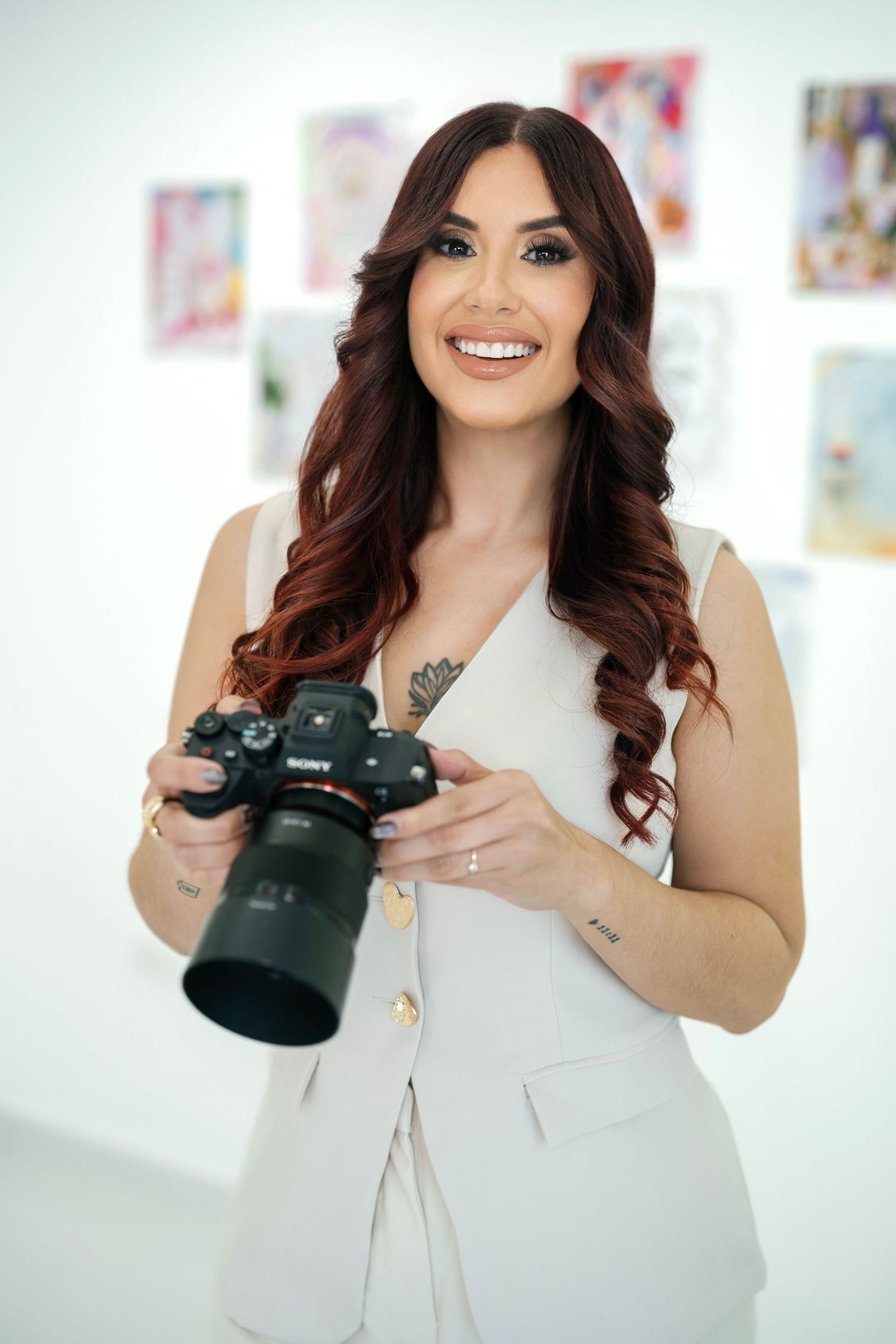 Professional holding DSLR camera while wearing cream-colored outfit in bright studio space.