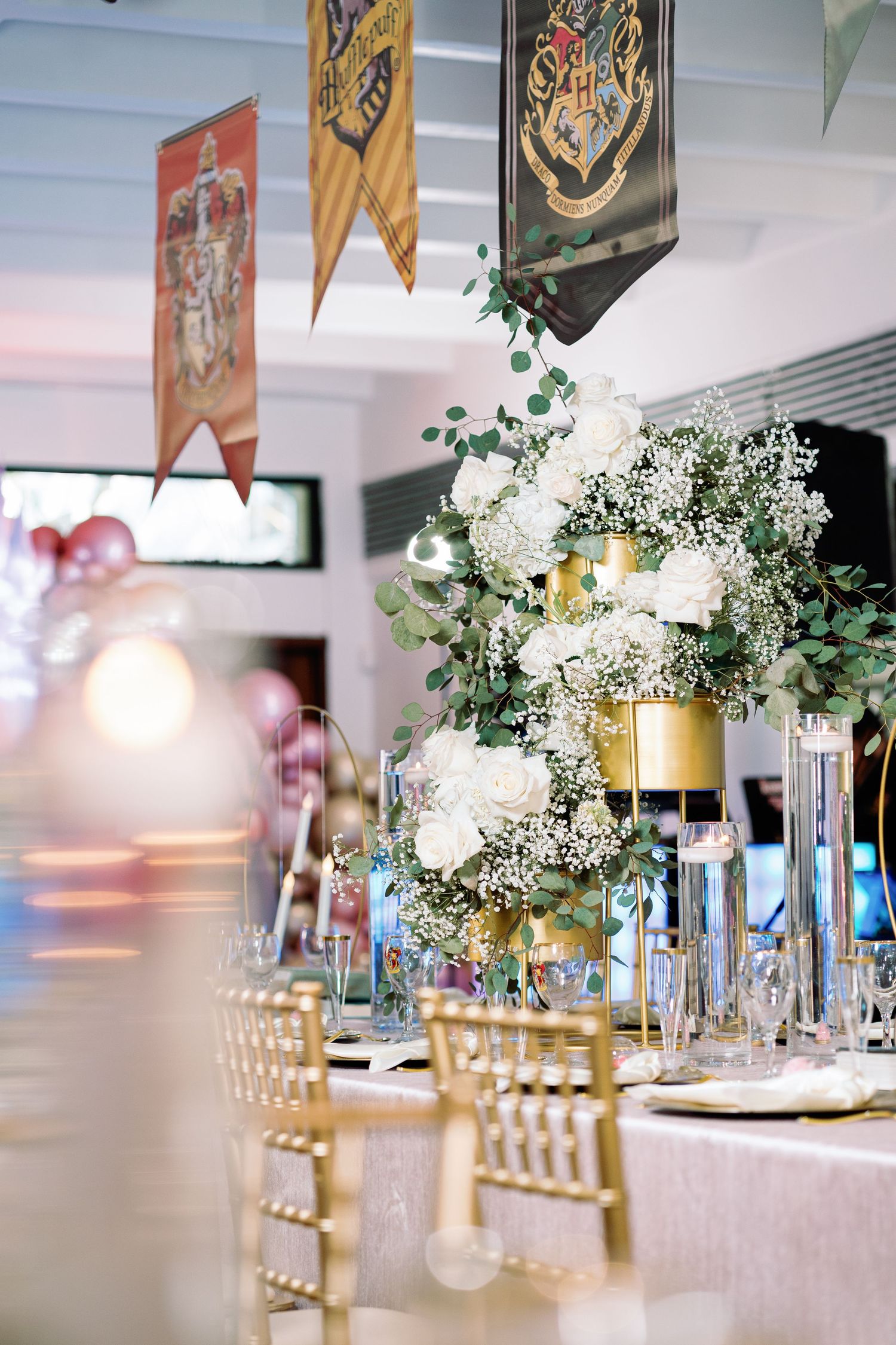Elegant wedding reception table setup with gold chairs and hanging banners in a bright venue.