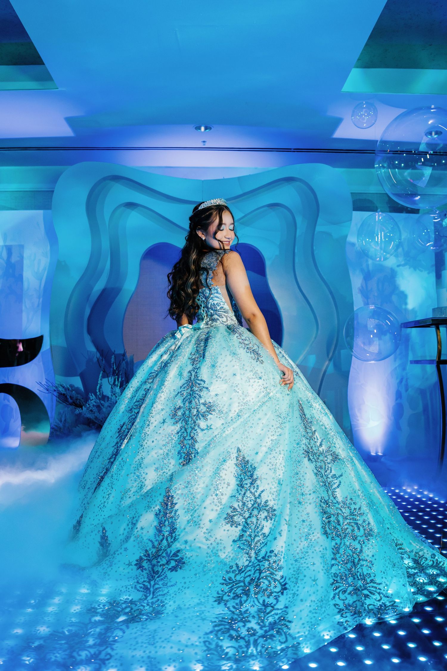 Sparkling turquoise ballgown photographed on illuminated dance floor with blue lighting.