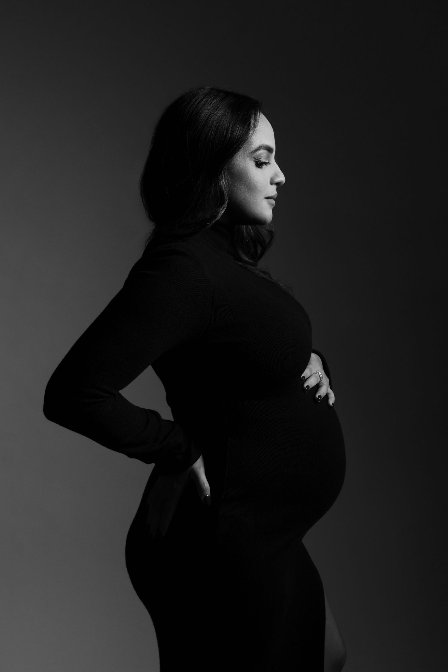 Artistic black and white profile portrait of an expectant mother in form-fitting dress.