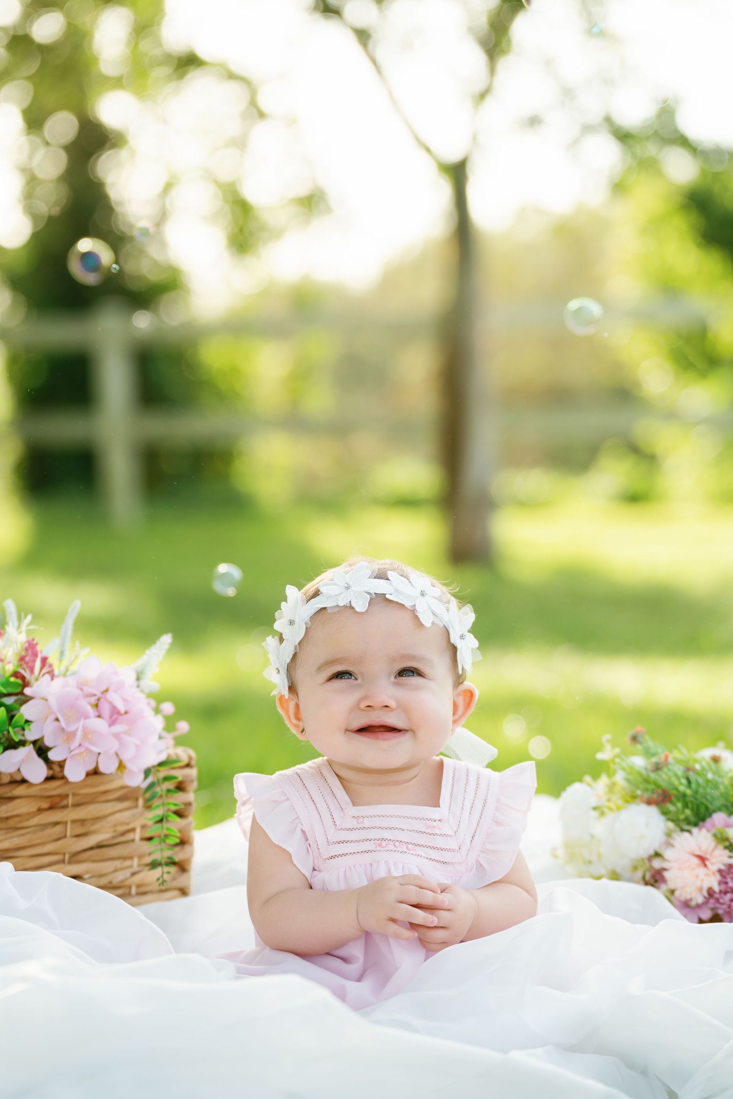 Baby milestone photo with flower crown and white dress surrounded by spring blooms.