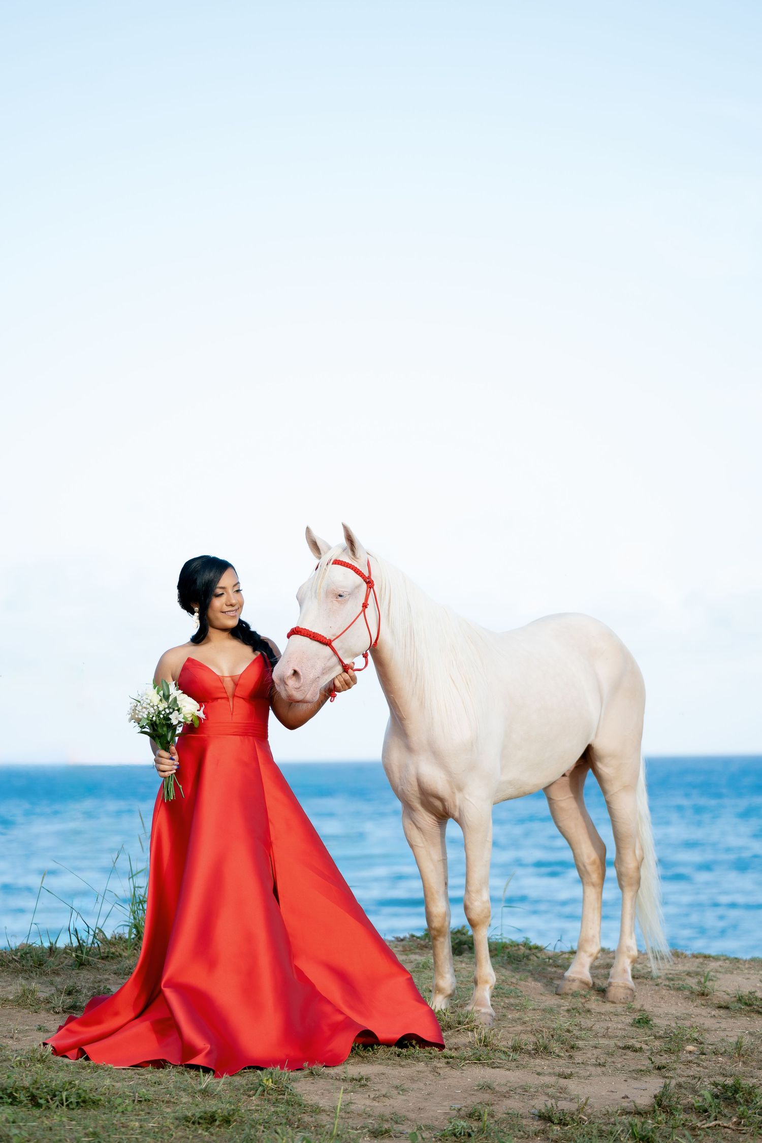 Dramatic red gown maternity photoshoot with white horses on a beach at sunset.