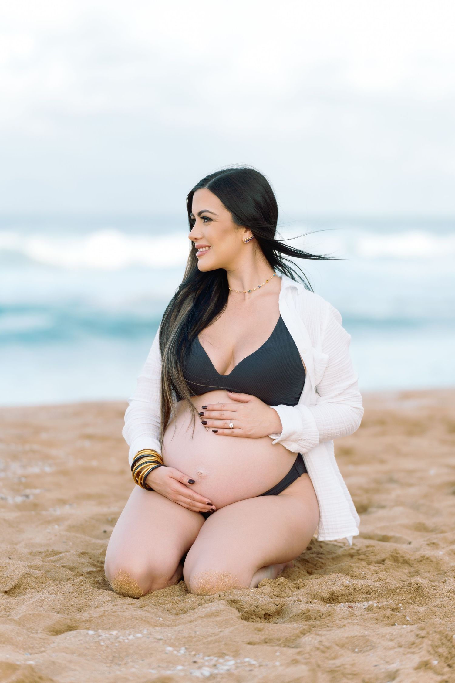 Maternity photoshoot on a sandy beach with waves in the background showing woman in black and white outfit.