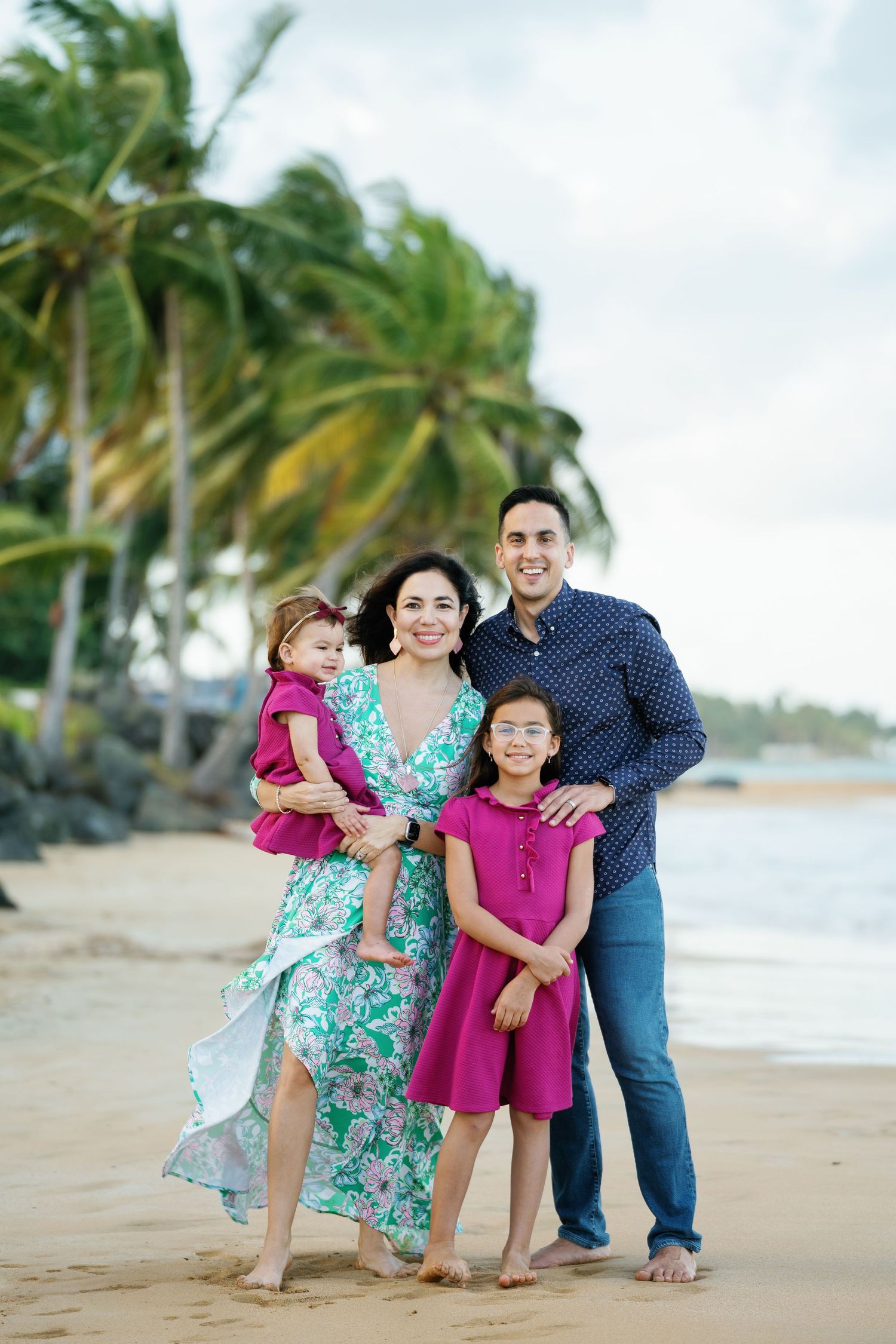 Family portrait session on a tropical beach with palm trees and casual coordinated outfits.