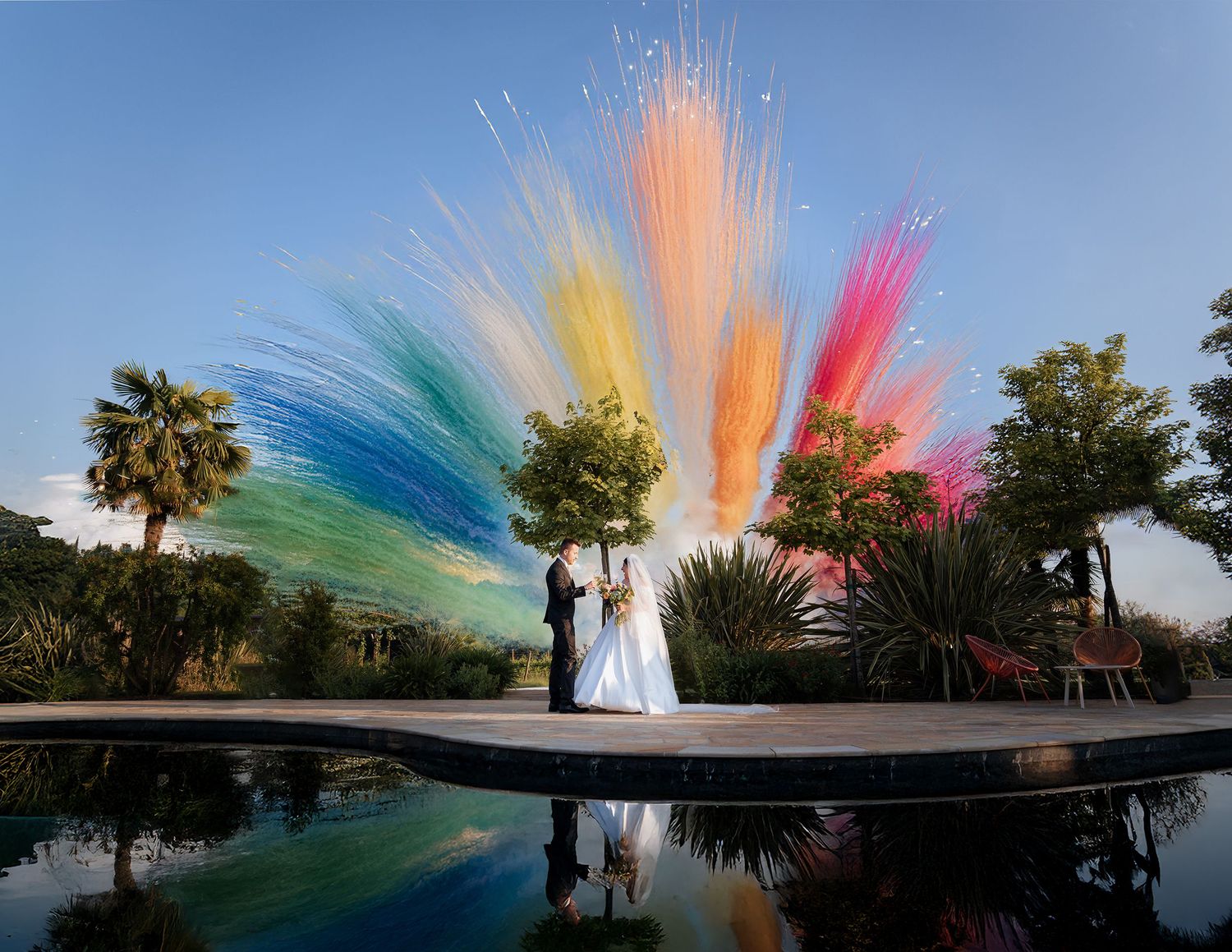 Colorful smoke bombs create a vibrant rainbow effect behind a couple during an outdoor wedding photo session at sunset.