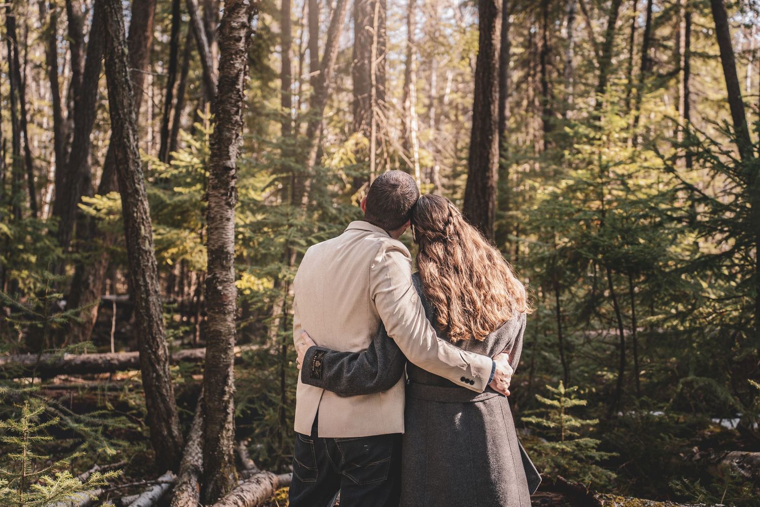 Romantic couple embracing and kissing from behind in lush green sunlit forest setting.