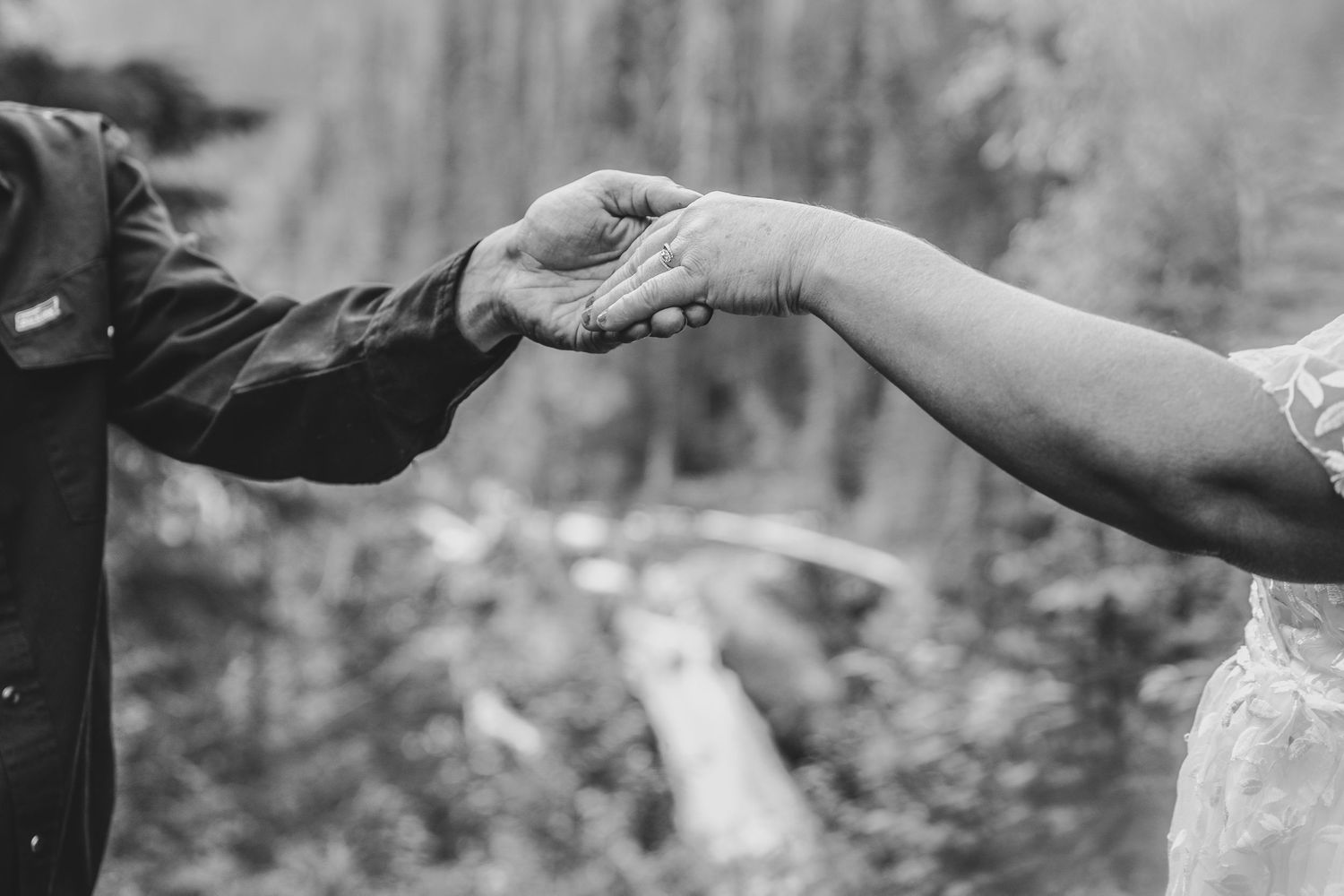 Black and white close-up of bride and groom holding hands tenderly during outdoor wedding ceremony.