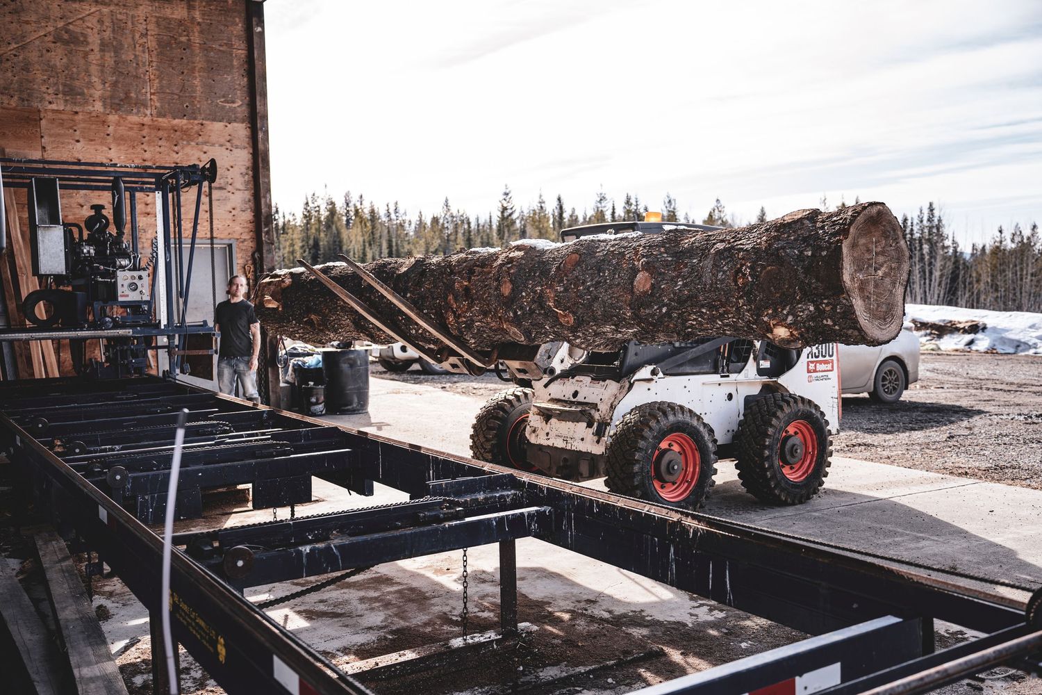 Bobcat skid steer loader moving large logs onto a flatbed trailer in winter during Commercial Business Branding photoshoot.