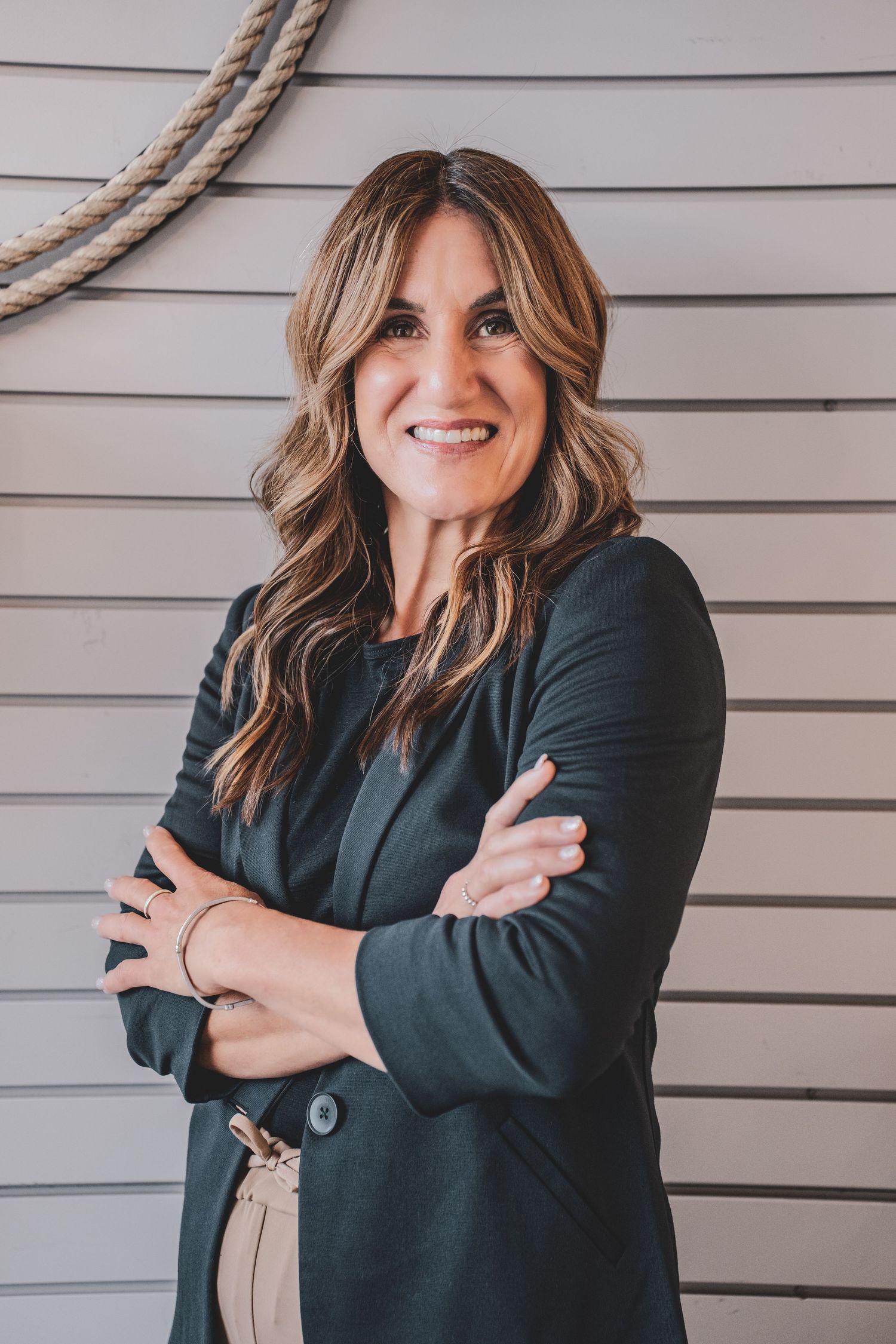 Confident brunette businesswoman smiling with arms crossed against a white shiplap wall.