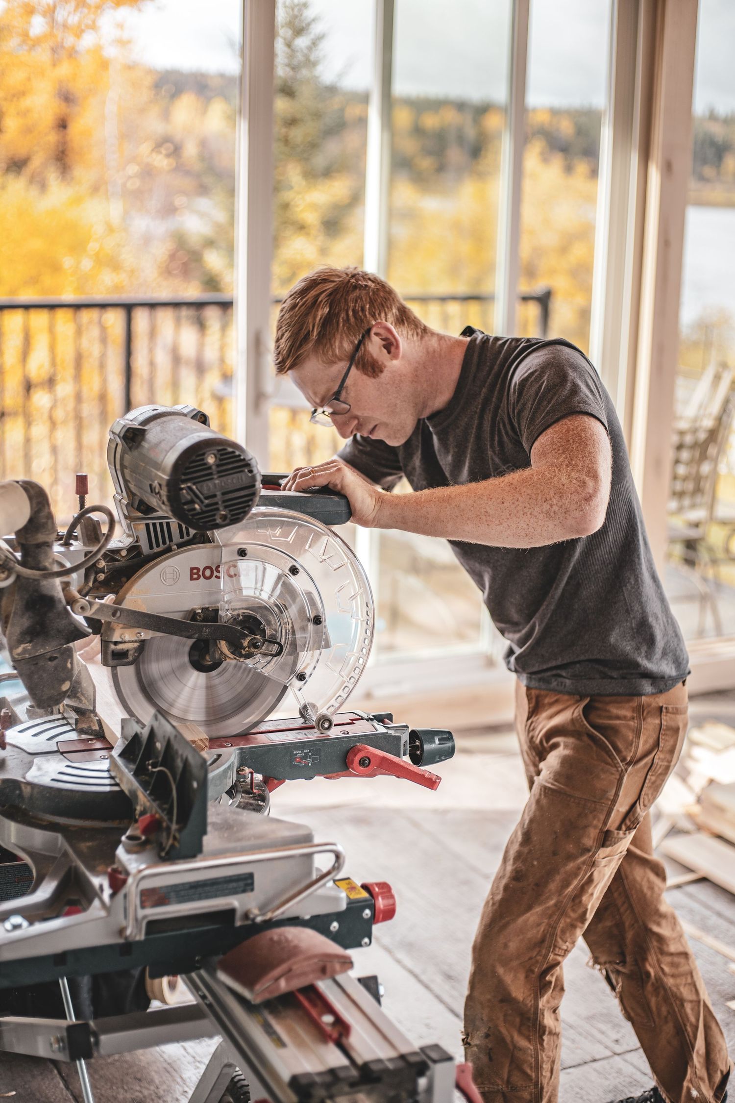 Young redhead man using Bosch miter saw during home construction with autumn view.